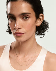Young woman wearing the Mini Serpentine Necklace, featuring light S-curve links, adding subtle shine and movement, complemented by simple gold hoop earrings.