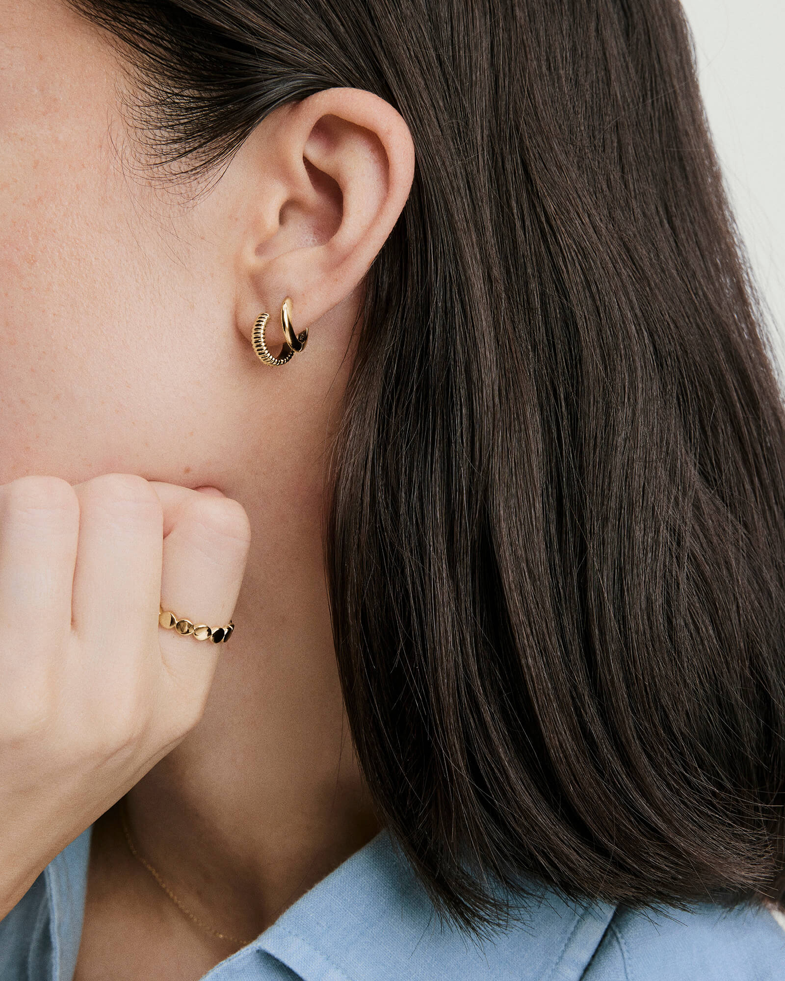 Close-up of a person wearing Charlotte Textured Huggie Hoops, highlighting the sculpted curves and polished finish of the petite, ridged gold hoop earrings.
