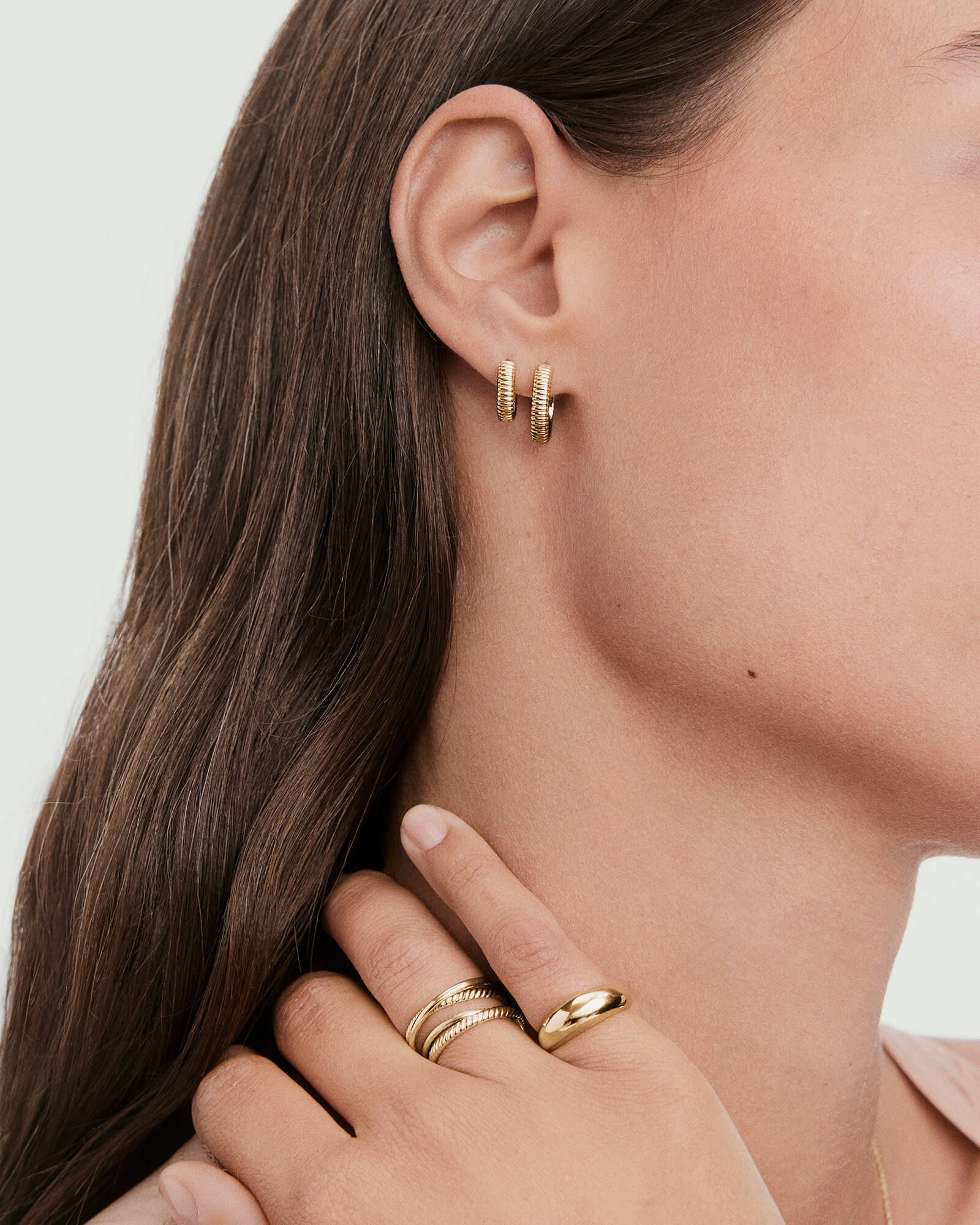 Charlotte Textured Hoops: Close-up of textured gold hoop earrings on a woman's ear, paired with gold rings, highlighting their modern, lightweight design.