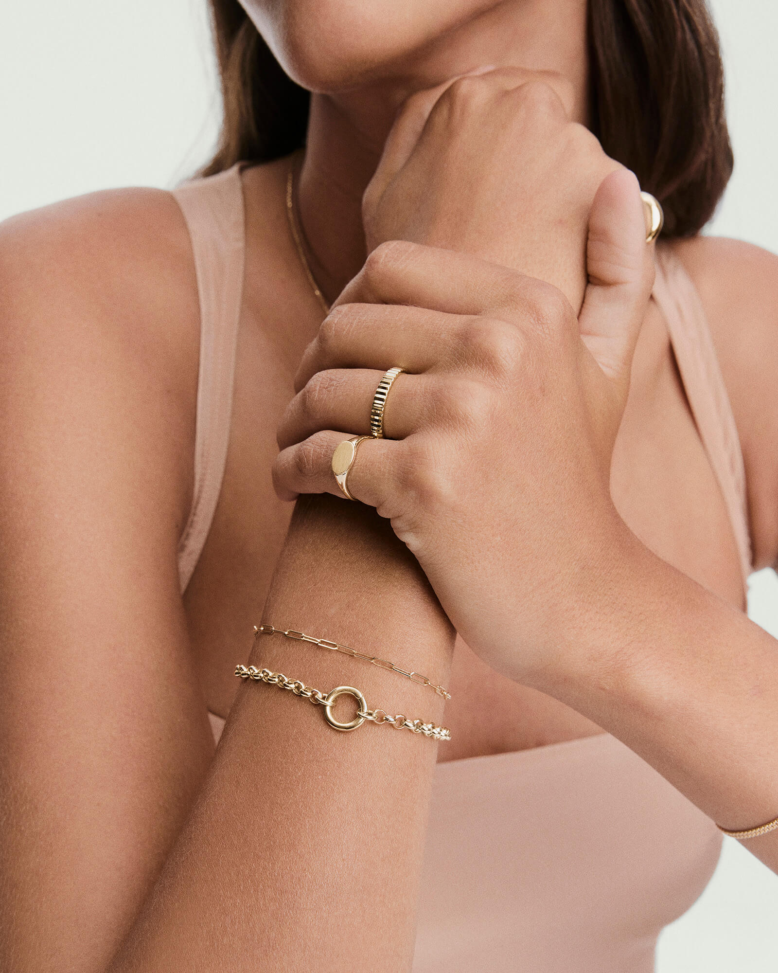 Woman's hands adorned with the Bold Eternity Line Band, featuring a fluted texture, alongside delicate gold bracelets and a smooth signet ring.