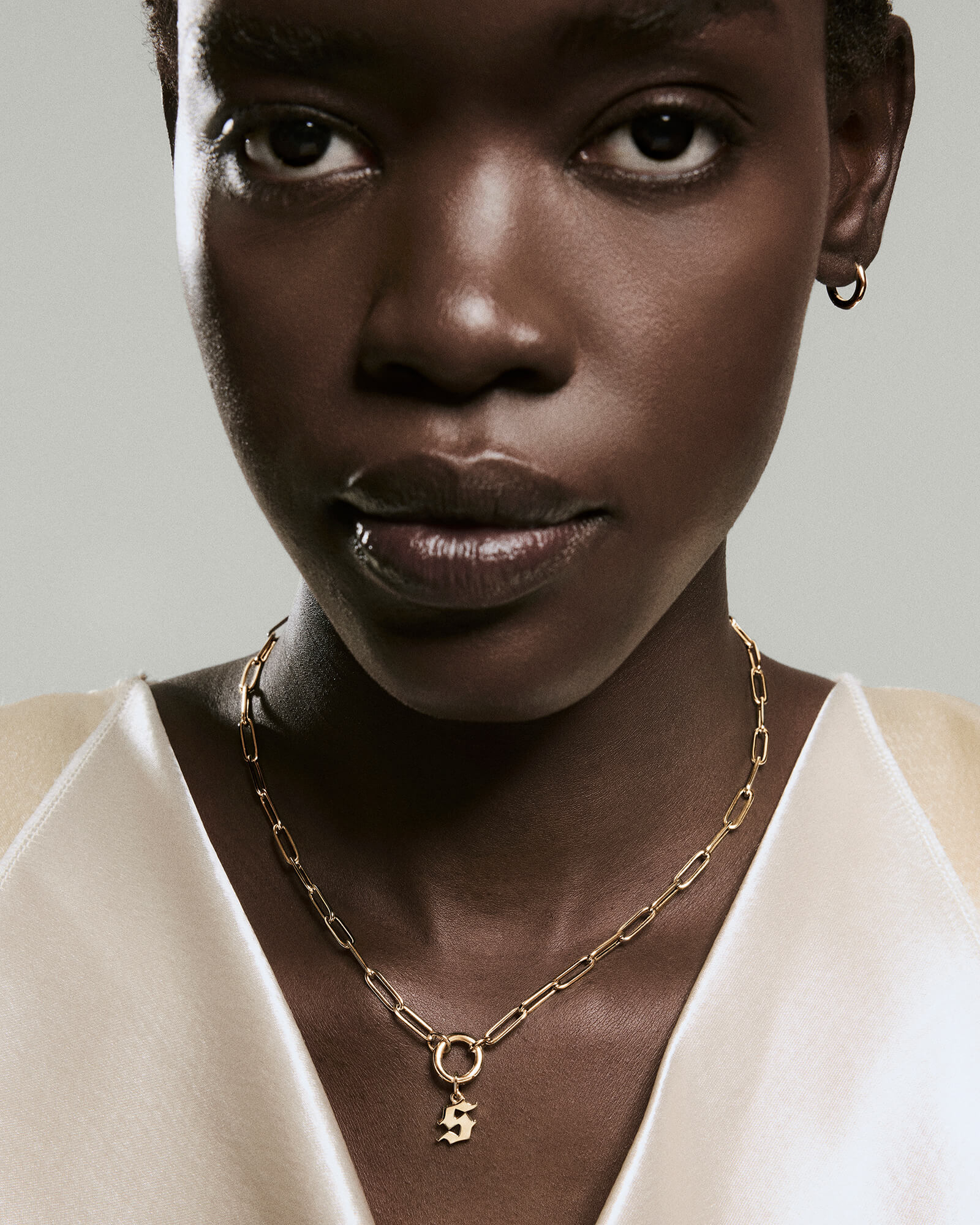Close-up of a woman wearing a Gothic Letter Pendant necklace with a gold chain and number 5 pendant, complemented by a gold hoop earring.