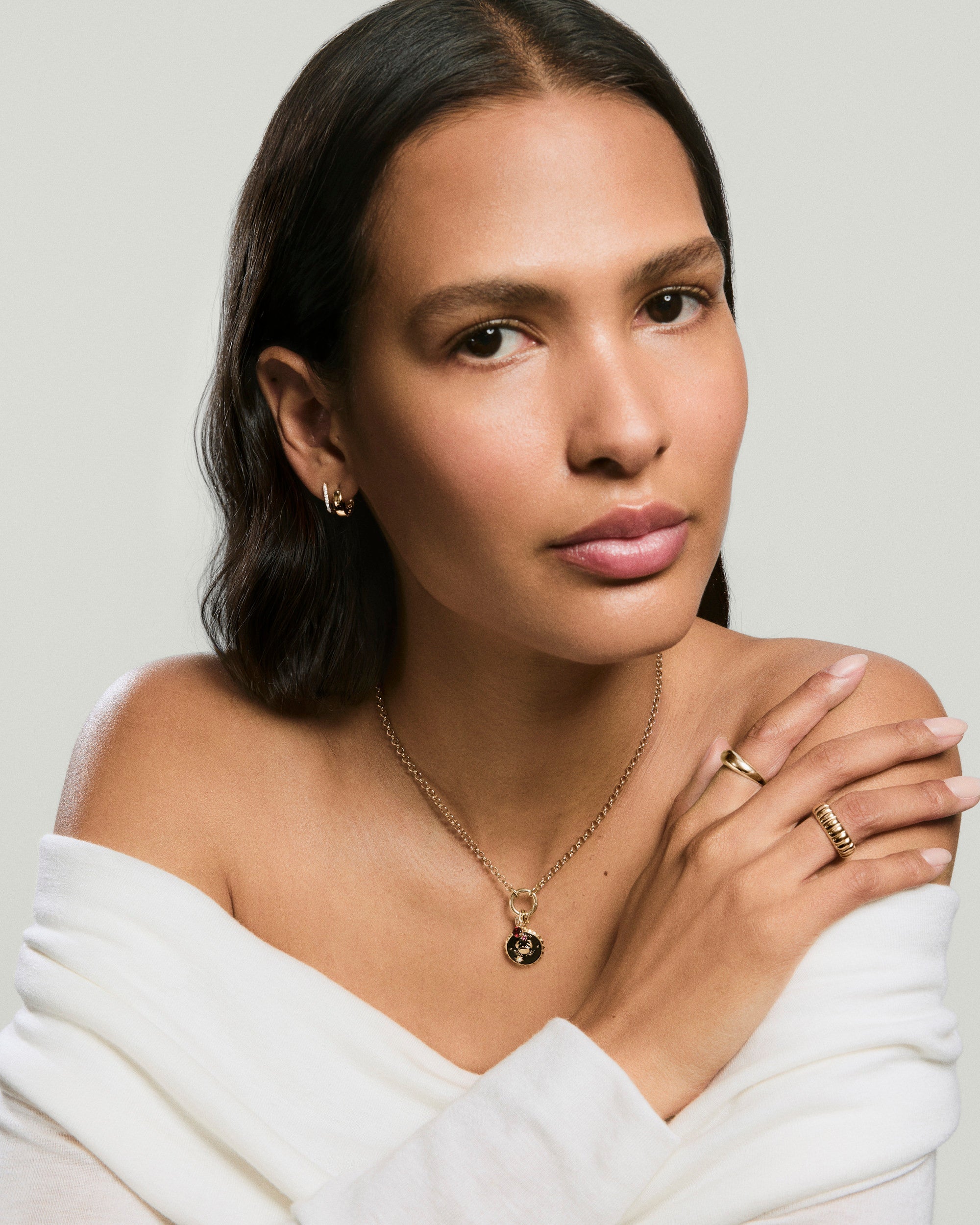 Woman wearing gold jewelry, showcasing the Cosmic Charm: a round pendant in precious metals and black enamel with gemstone accents, reflecting celestial elegance.