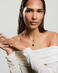 Woman modeling Cosmic Pendant Necklace with layered gold chains; one with a coin-style pendant. Also wearing a chunky ring, slim band, and gold hoop earrings.