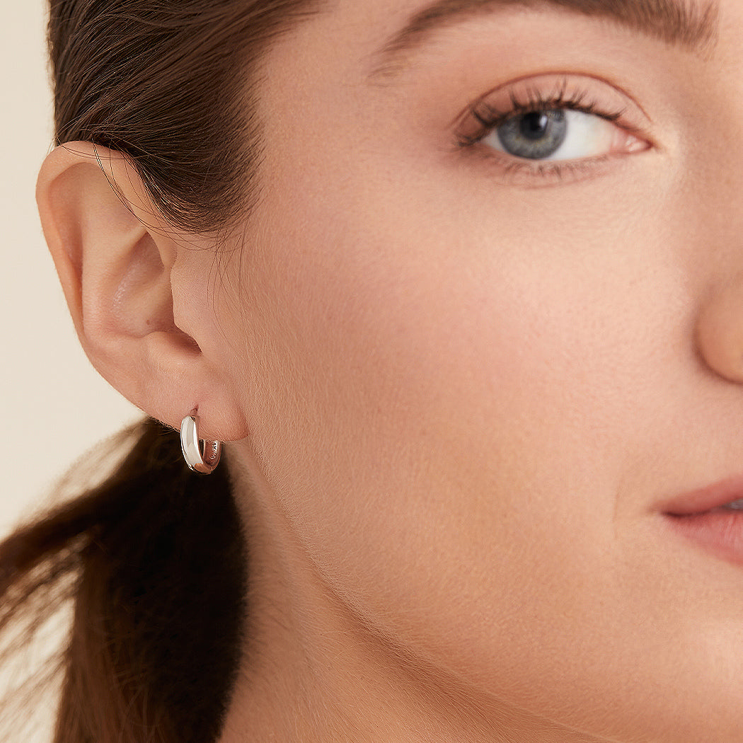 Close-up of a woman's face wearing Bold Huggie Hoops, showcasing the earrings' sleek design and how they elevate her look.