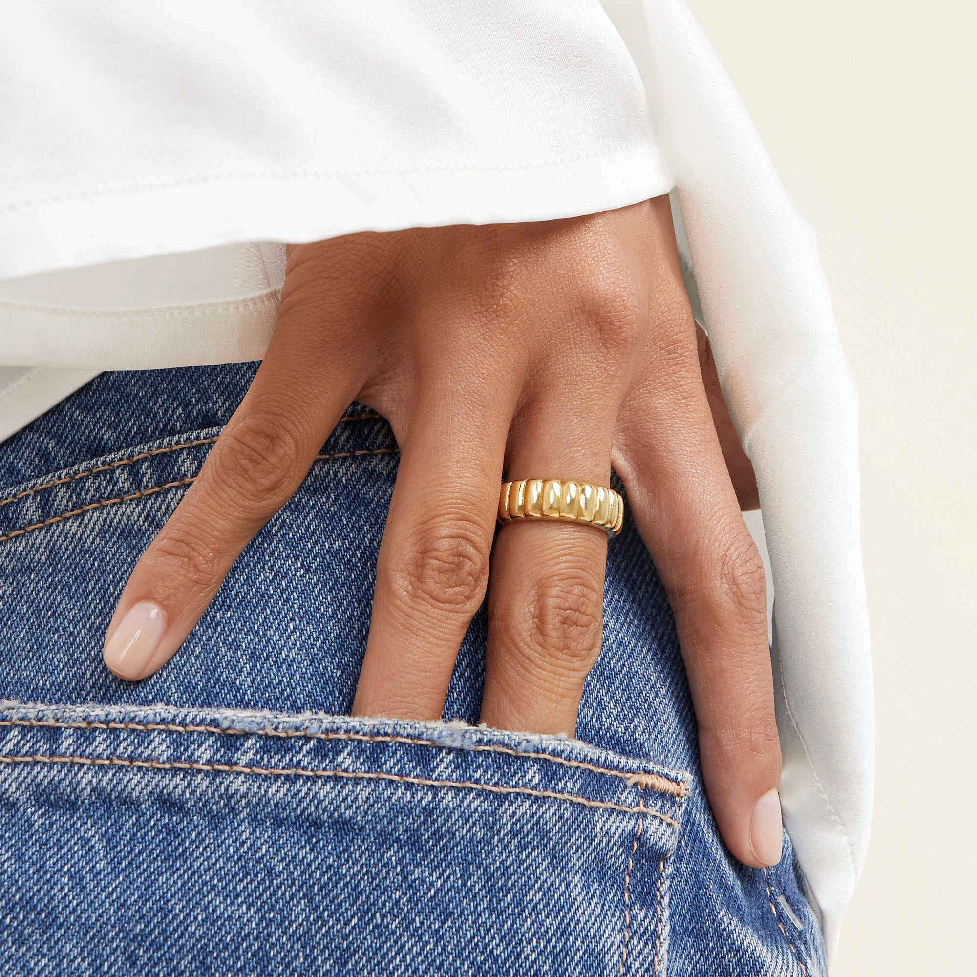 Hand wearing the Charlotte Ring, a gold accessory, partially tucked into the pocket of blue jeans.