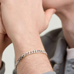Person wearing a Curb Chain Bracelet, a sleek silver accessory designed for everyday wear, shown on a man's wrist for a stylish, modern look.