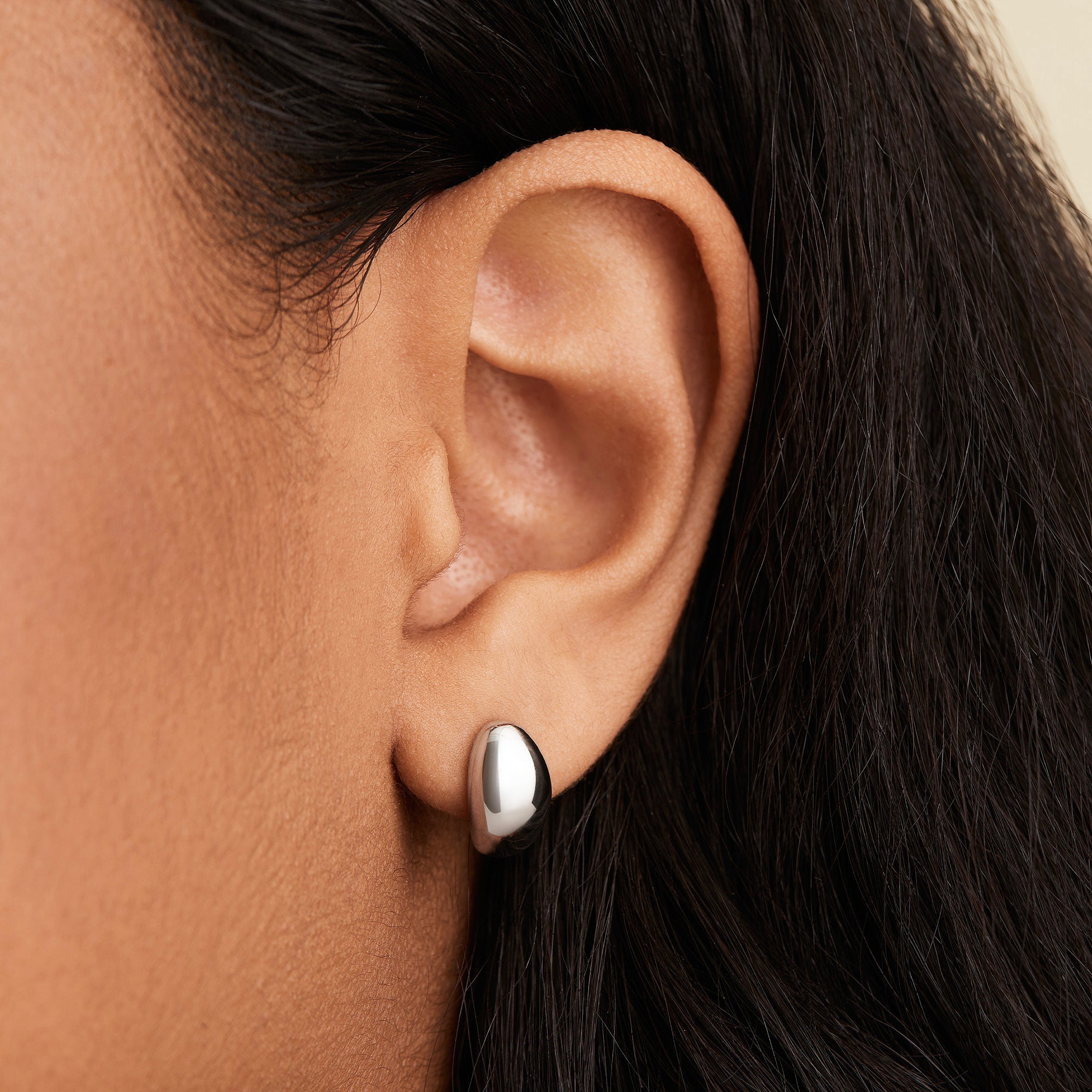 Close-up of a woman's ear wearing Mejuri DÃ´me Huggies, showcasing the sleek, sculptural design of the lobe-hugging earrings from the iconic collection.