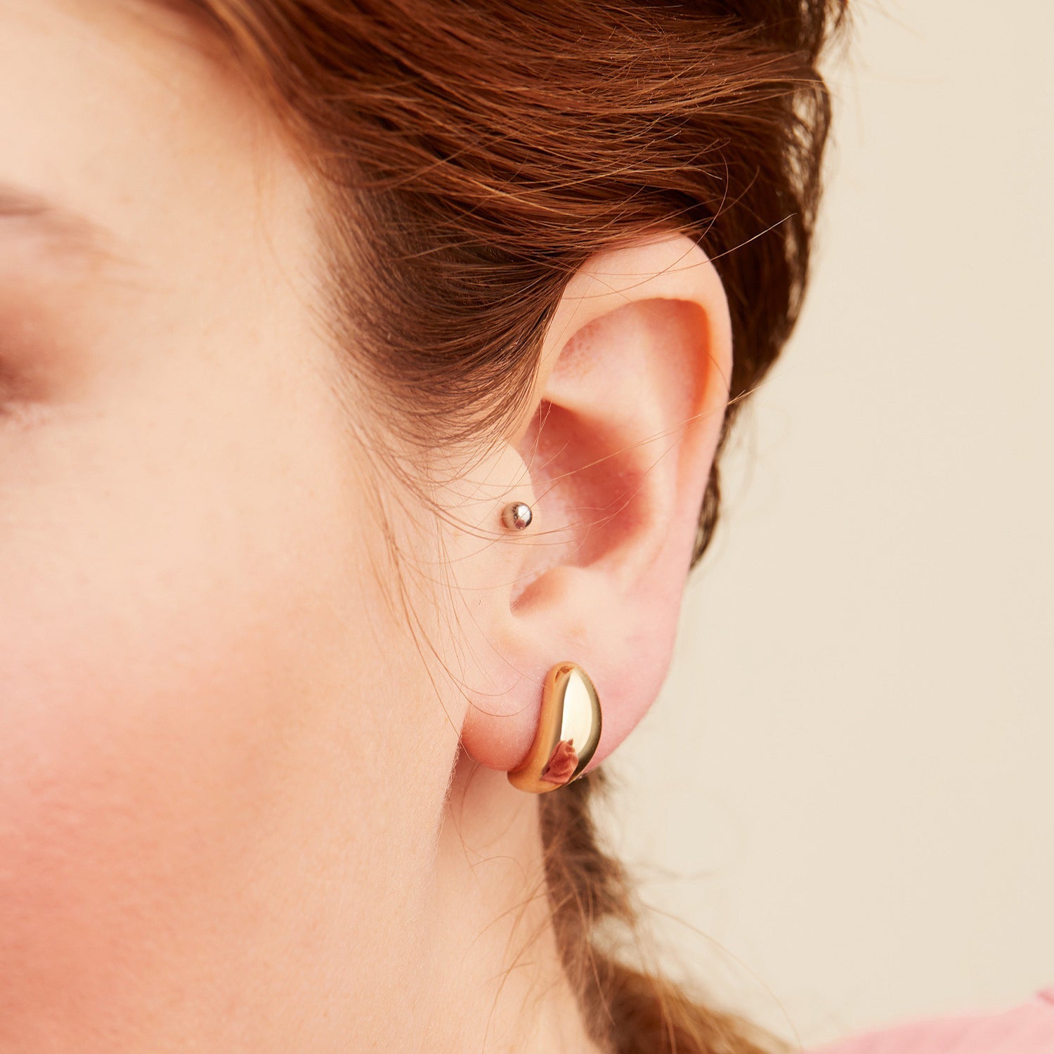 Close-up of a woman's ear wearing Mejuri DÃ´me Huggies, showcasing their sleek, sculptural style and lobe-hugging design from the iconic DÃ´me collection.