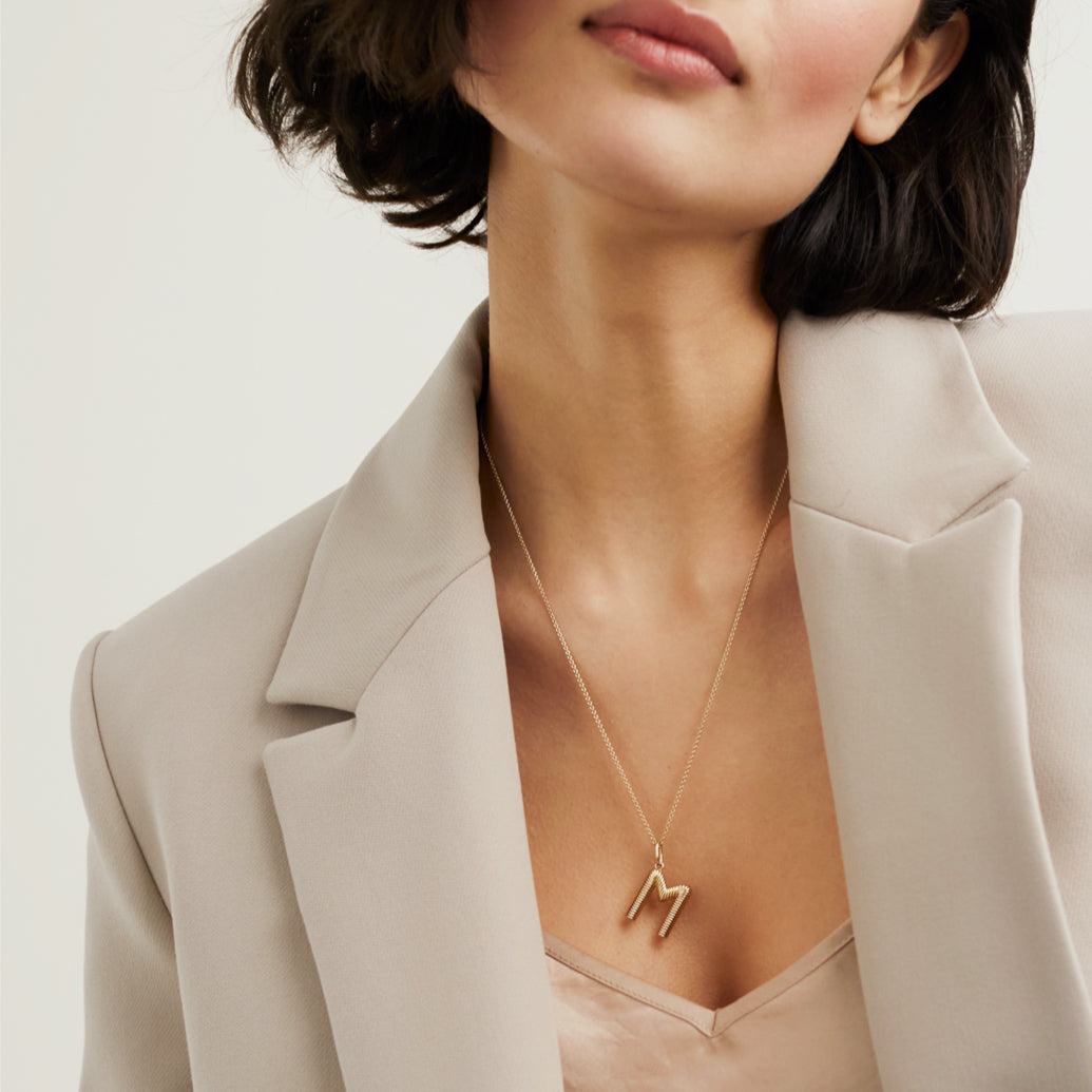 Woman wearing Bold Letter Pendant Necklace in 18k gold vermeil with an accordion pattern on a 20 to 22-inch cable chain.