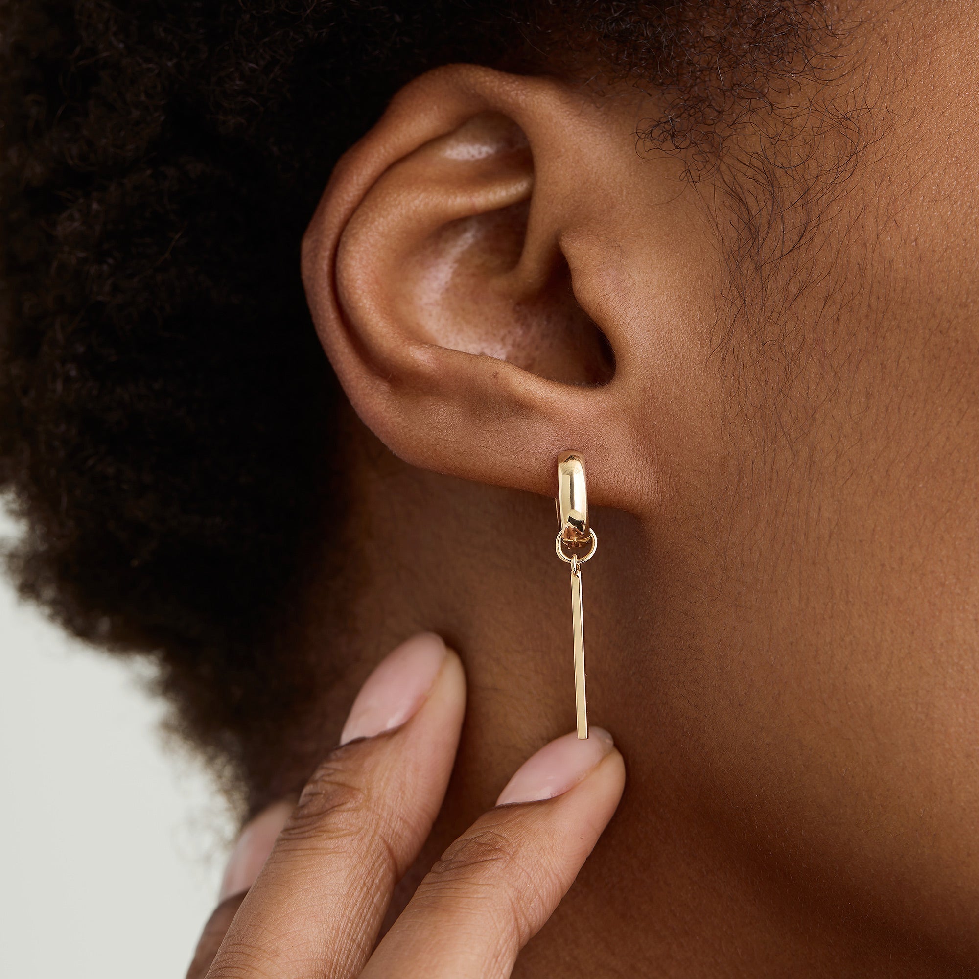 Person touching an earring with a Single Bar Hoop Charm, showcasing a sleek, rectangular design perfect for personalizing everyday hoops with interchangeable charms.