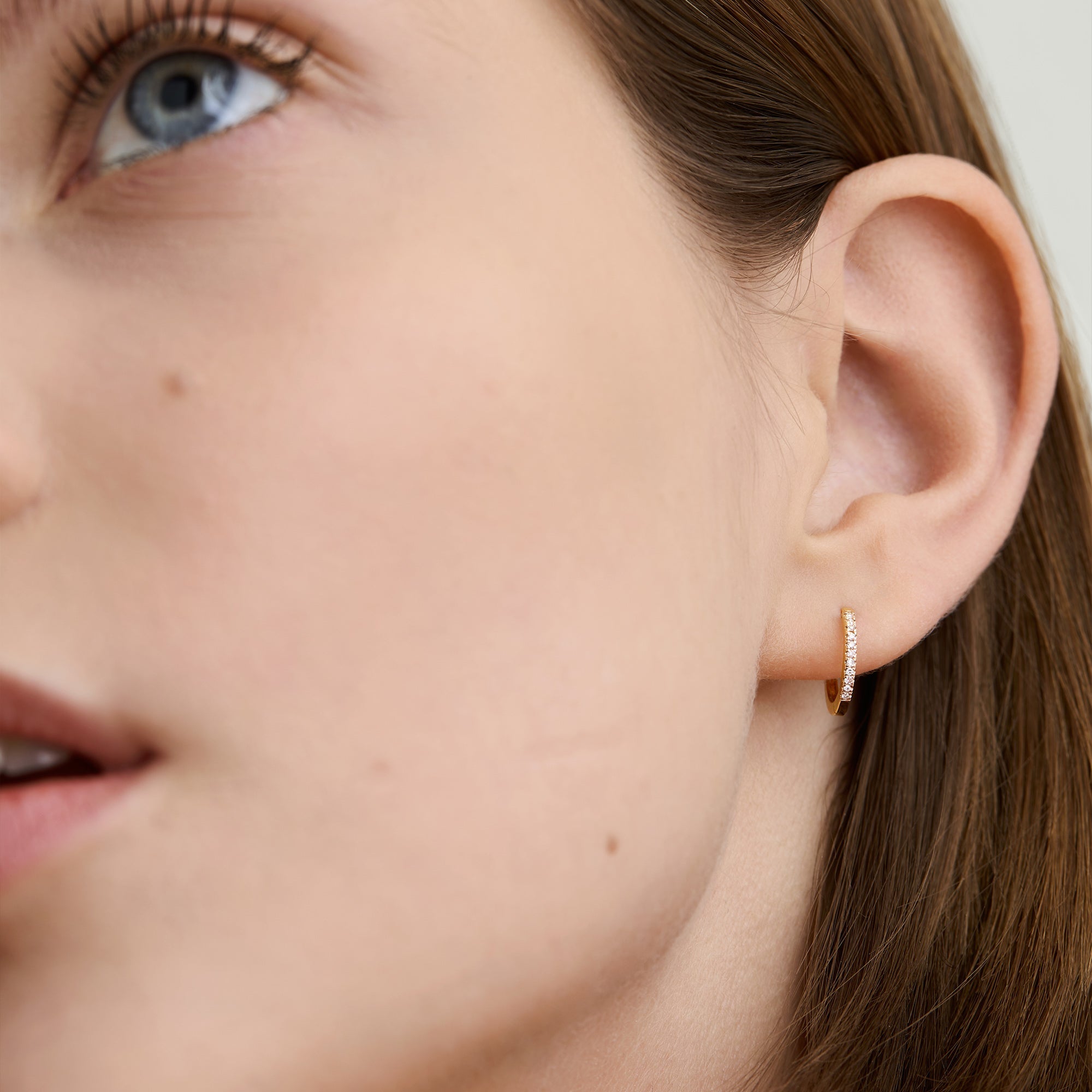 Close-up of a woman's ear wearing the Single PavÃ© Diamond Huggie Hoop, a handcrafted 14k solid gold earring with pavÃ© diamonds.