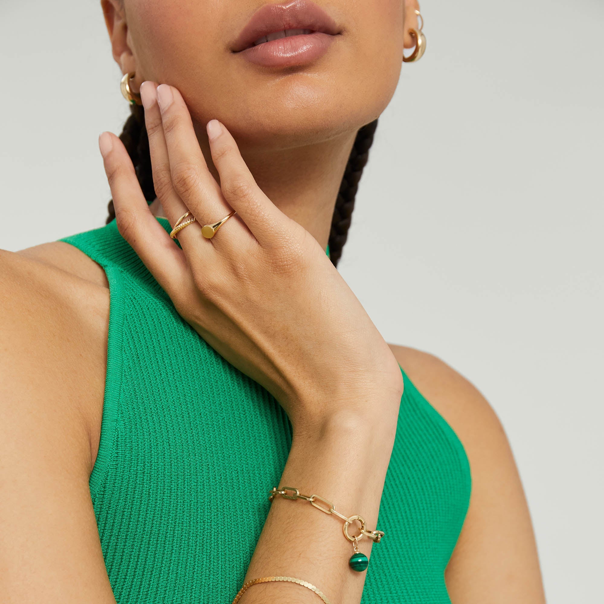 Woman wearing a green dress and gold jewelry, featuring the Paperclip Chain Charm Bracelet with a Stacker Clasp, showcasing layered charms.