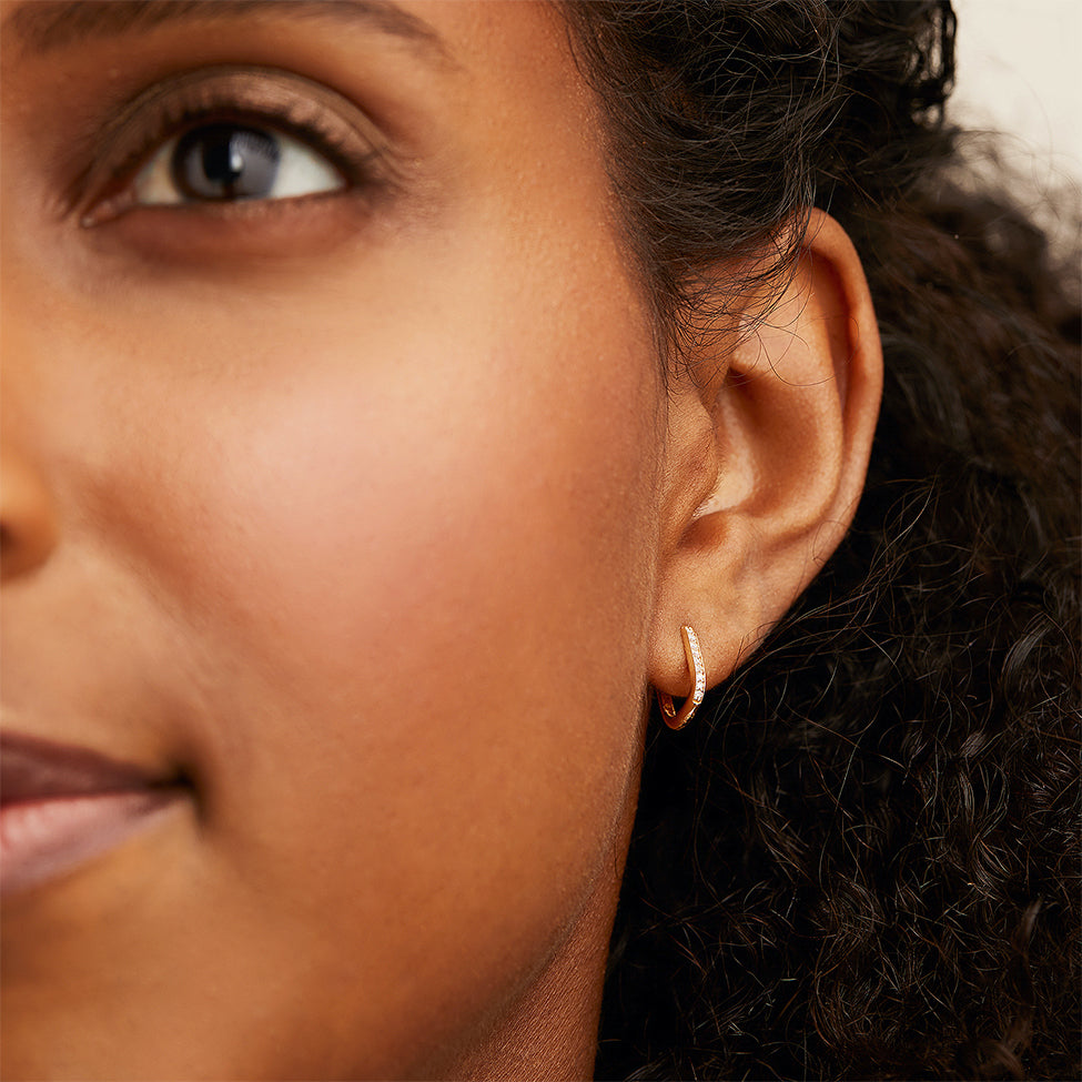 Close-up of a woman's ear wearing a Single PavÃ© Diamond Huggie U Hoop, featuring a sparkly design in 14k solid gold with responsibly sourced diamonds.