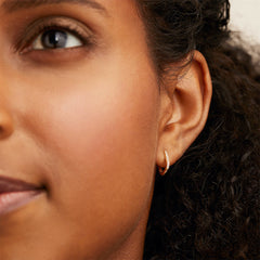 Close-up of a woman's ear wearing a Single PavÃ© Diamond Huggie U Hoop, featuring a sparkly design in 14k solid gold with responsibly sourced diamonds.