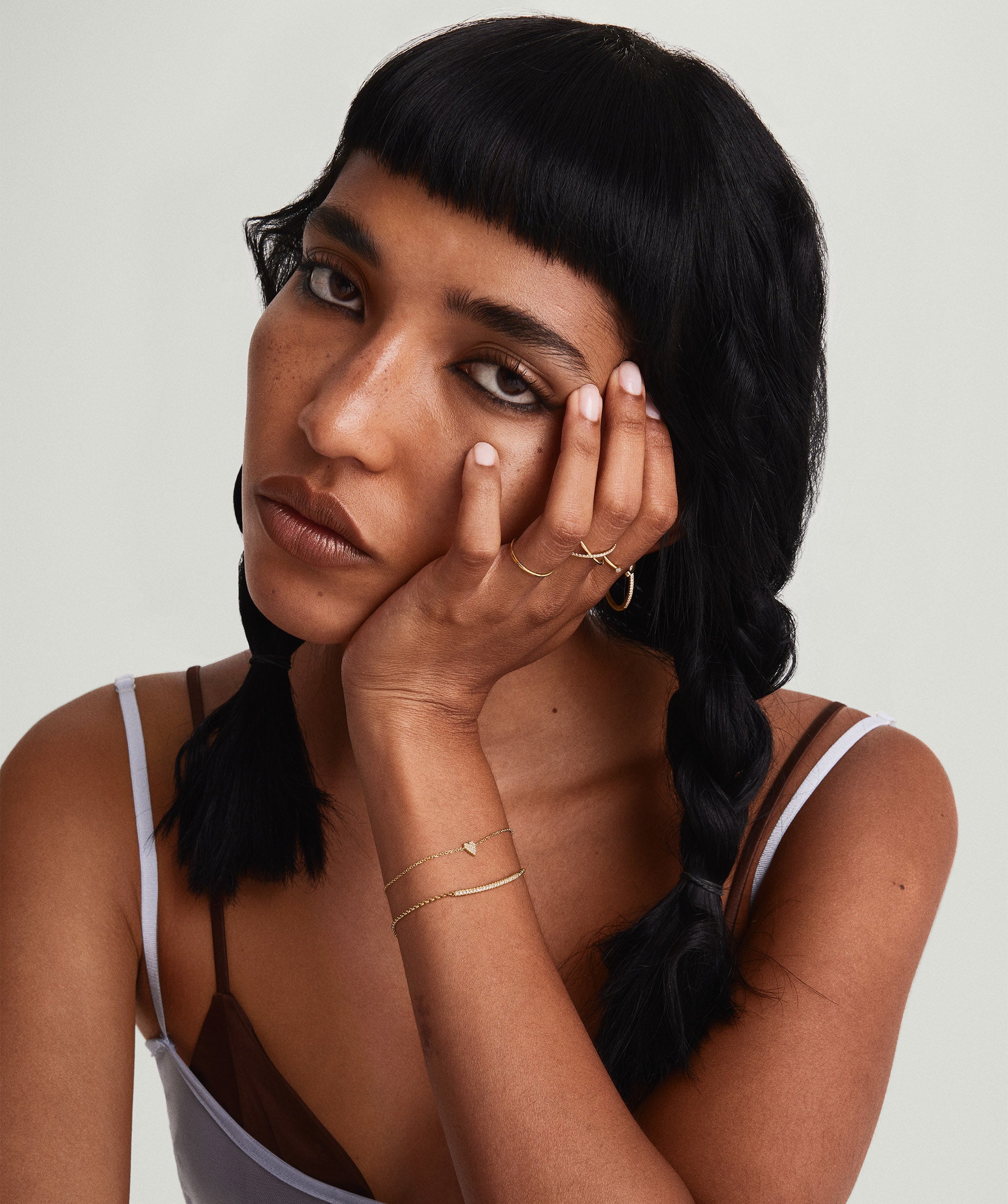 Woman with braided hair, hand on face, showcasing Mini Heart PavÃ© Diamond Bracelet on wrist.