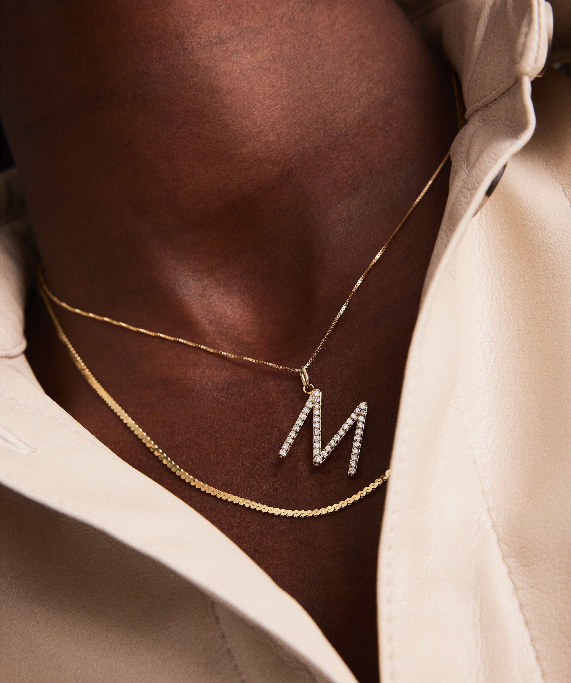 Person wearing a 14k gold necklace with an oversized letter charm, adorned with lab-grown diamonds.