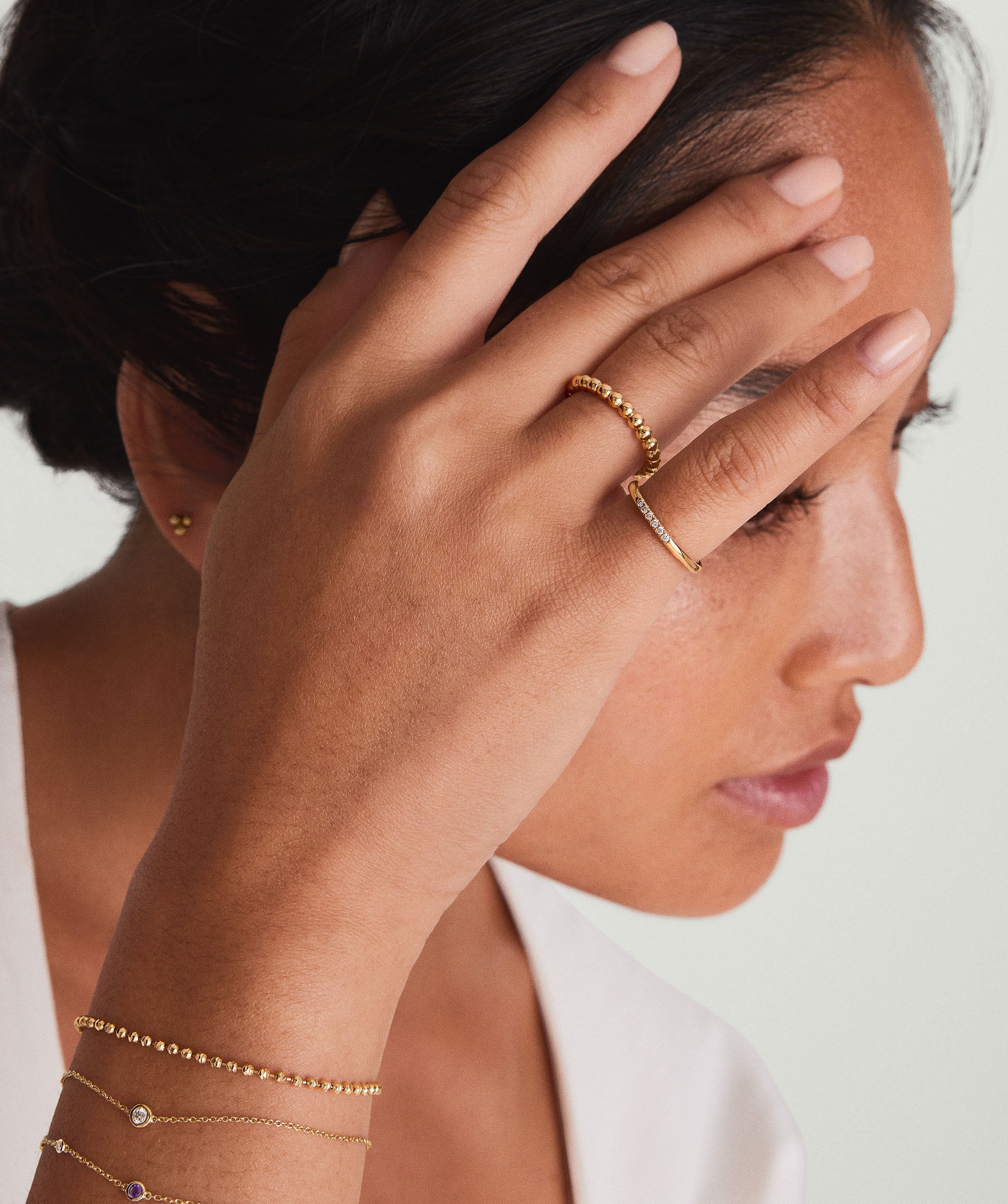 A woman wearing the Diamonds Line Ring and a gold bracelet, showcasing six responsibly sourced diamonds in a 14k solid gold prong setting.