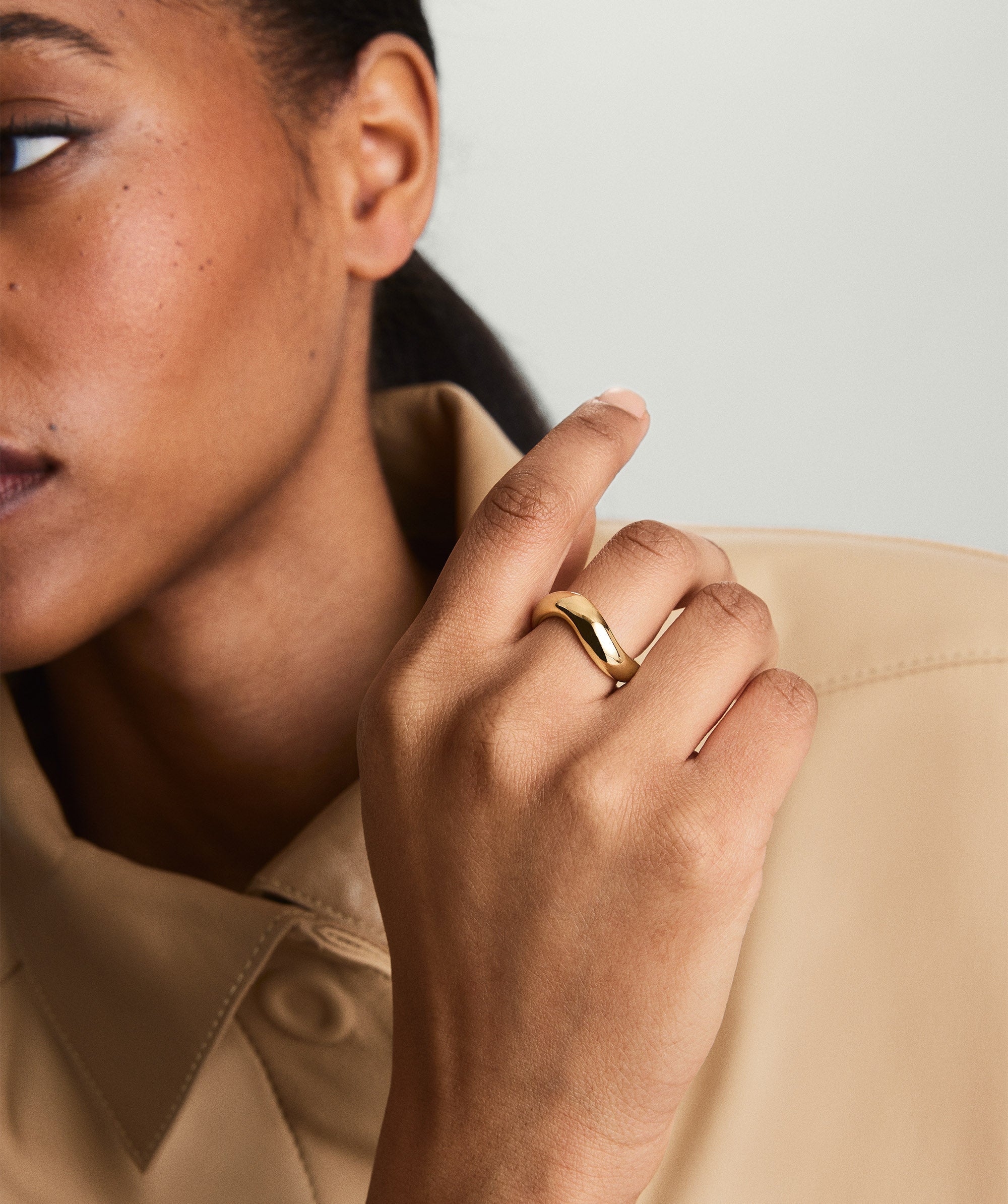 A woman wearing the DÃ´me Figure Ring, a gold ring with unique curves, showcased on her finger.