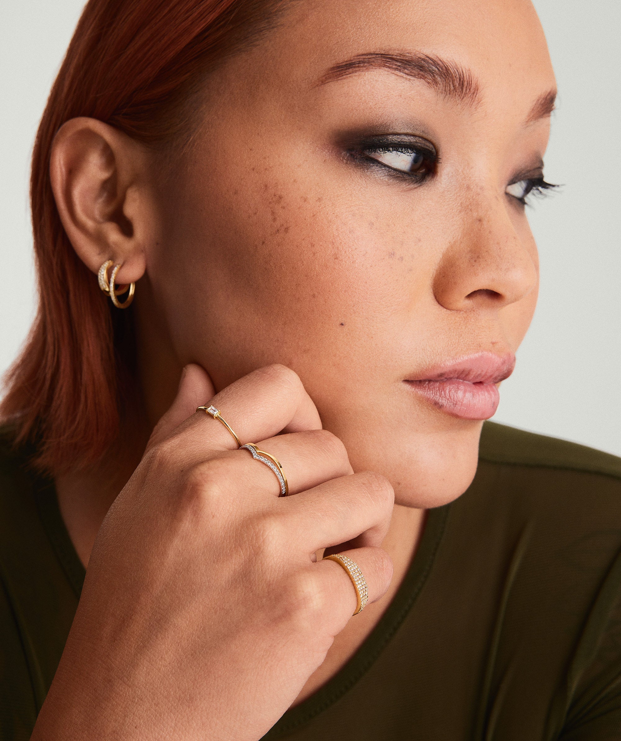Woman with red hair wearing a green shirt, showcasing a Baguette Stacker Ring on her finger, highlighted among other gold accessories.