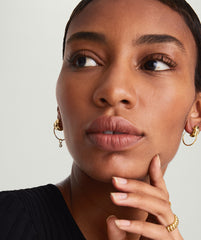 Woman contemplating, wearing handcrafted 14k solid gold Between Hoops. Light, hollow design suited for daily wear, even while swimming.