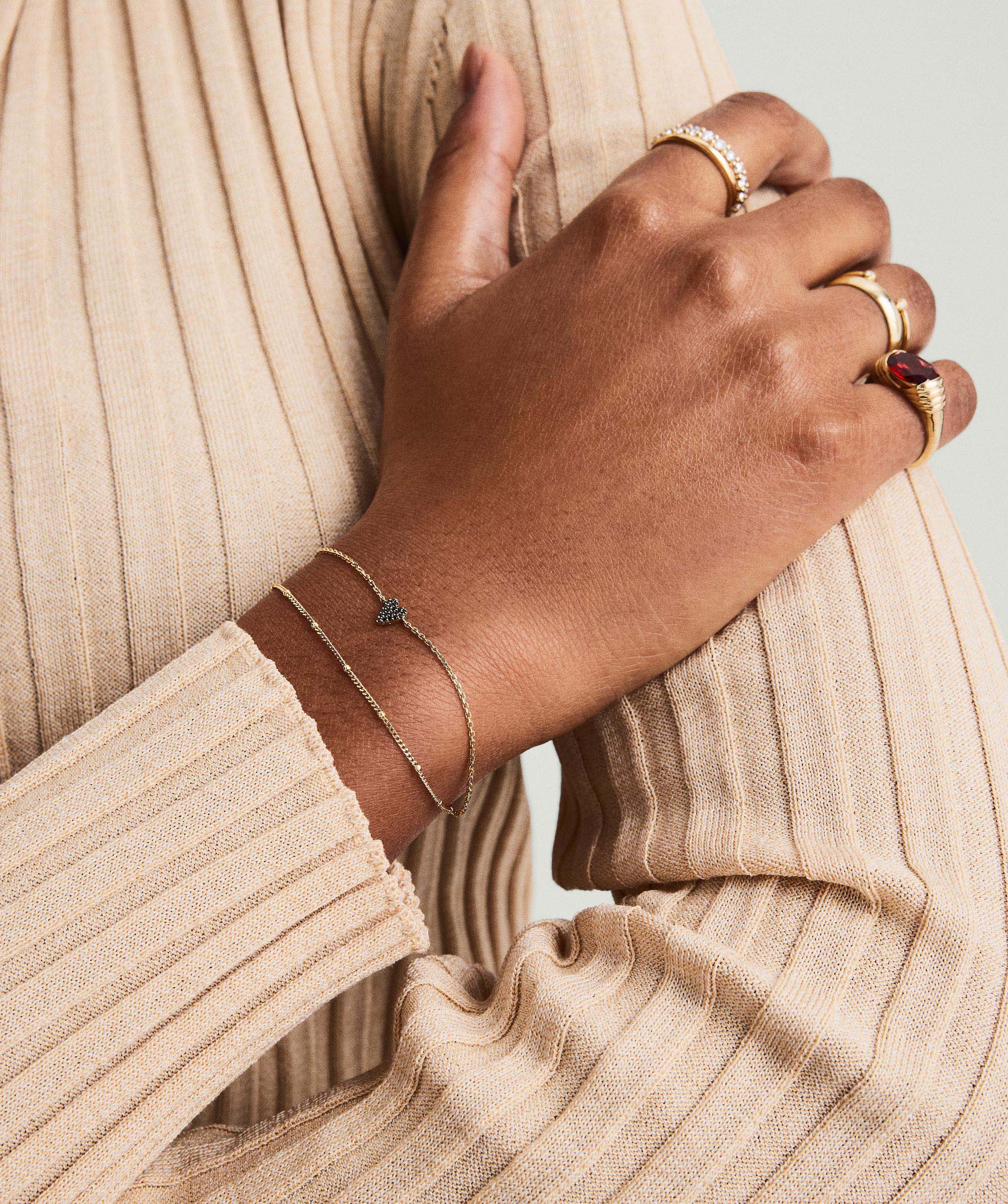 Close-up of a hand wearing the Mini Heart PavÃ© Diamond Bracelet, showcasing gold jewelry details on wrist and fingers.