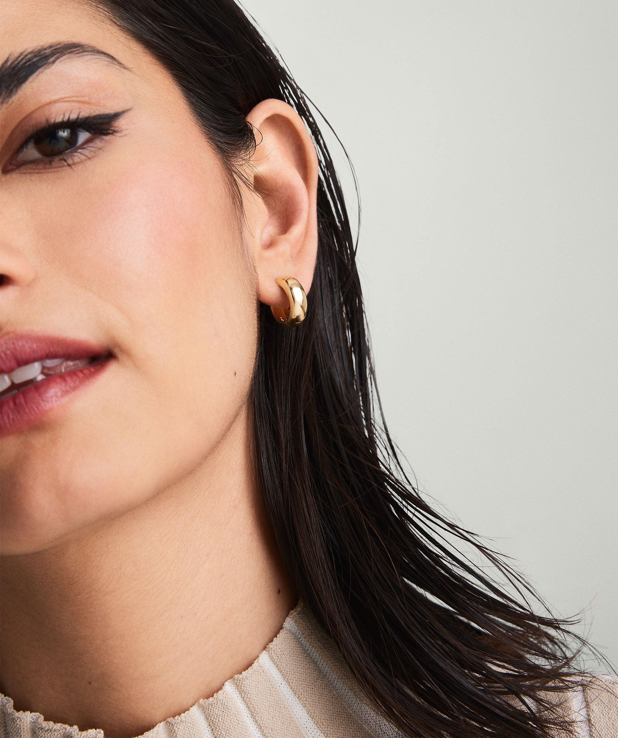 Close-up of a woman's face showcasing Plush Small Hoops, 14k solid gold earrings, elegantly adorning her earlobes.