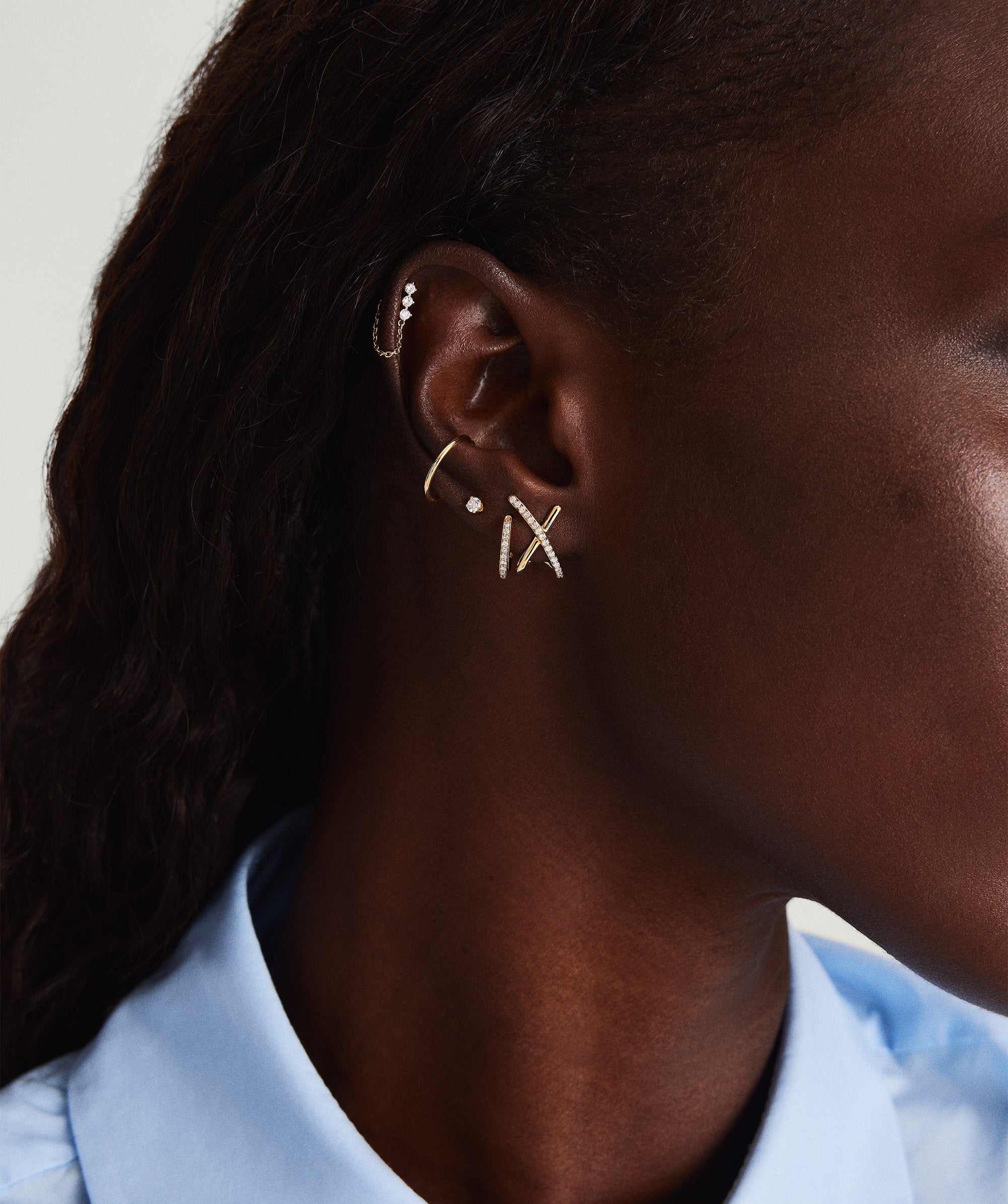 Close-up of a woman's ear wearing PavÃ© Diamond X Oversized Studs, handcrafted in 14k gold with pavÃ© diamonds, showcasing a gentle overlap design.