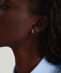 Close-up of a woman's ear wearing PavÃ© Diamond X Studs, handcrafted in 14k gold with pavÃ© diamonds, showcasing tubular lines overlapping gently.