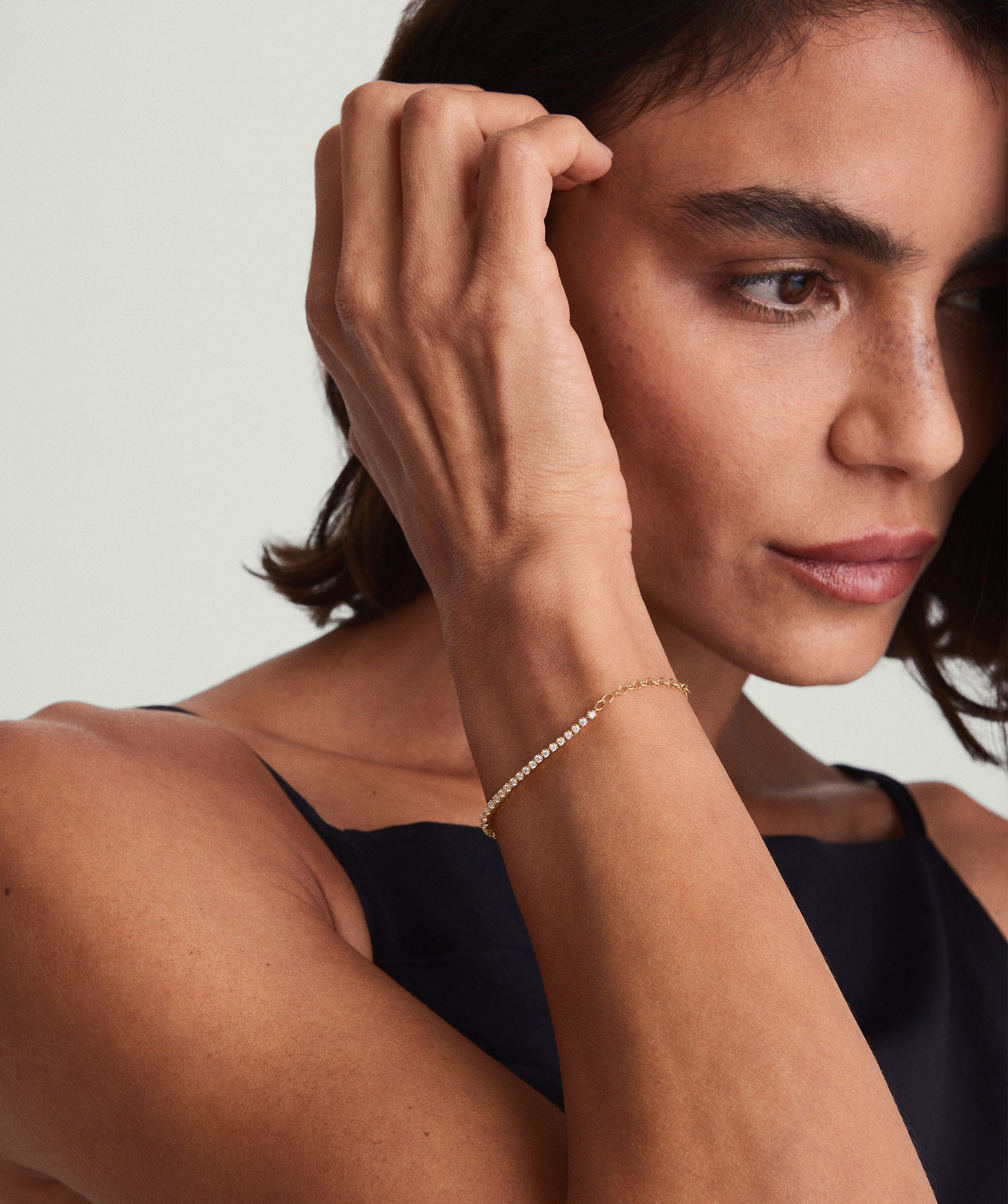 Woman wearing a black dress showcasing a Diamond Half Tennis Bracelet on her wrist, featuring a close-up view of the gold and diamond details.
