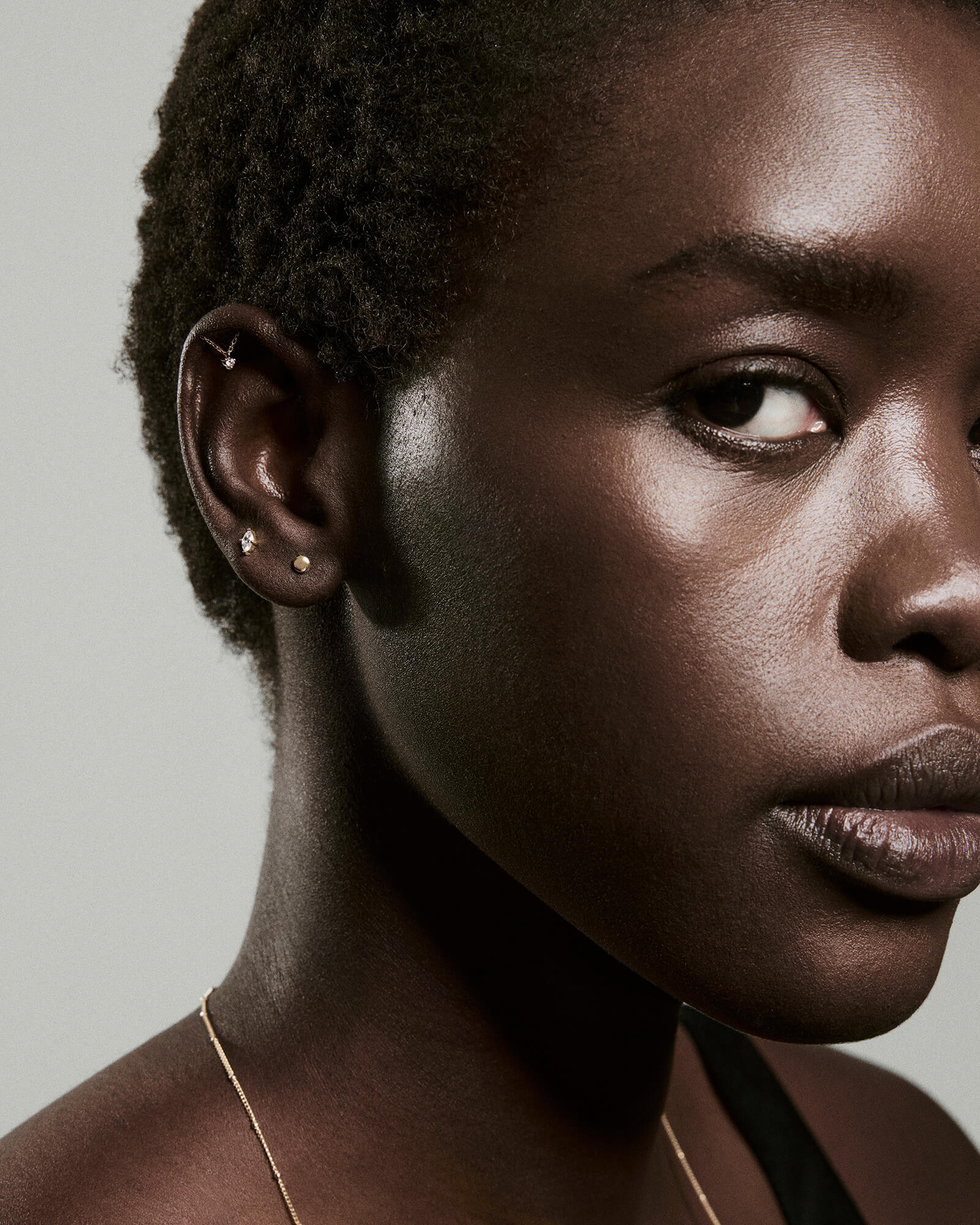 Close-up of marquise studs featured in a cluster of gold earrings on a dark-skinned person, highlighting the studs' edgy elegance and subtle stacking potential.