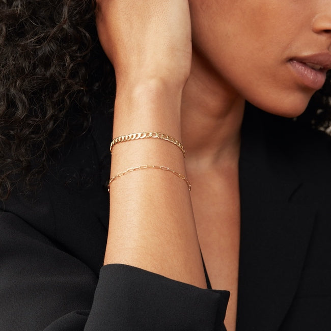 Woman wearing the Flat Curb Chain Bracelet, a versatile gold accessory that enhances any look, shown on her wrist in a close-up view.