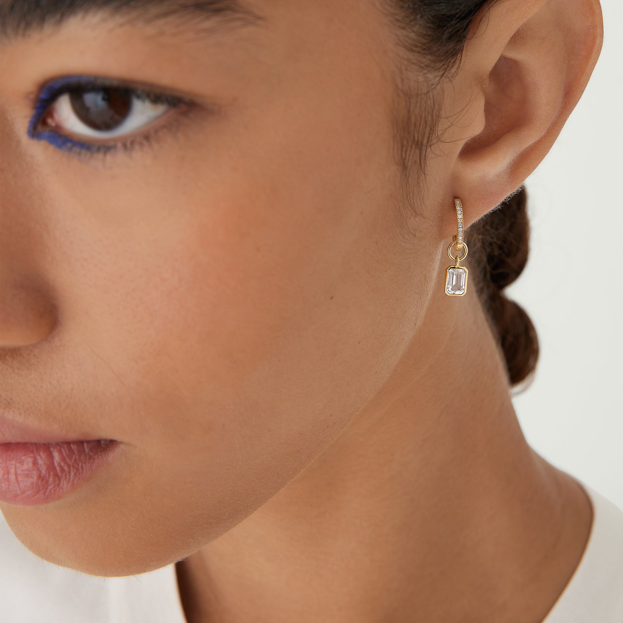Close-up of a woman's ear wearing a Single Emerald Cut Gemstone Hoop Charm, showcasing the elegant and personalized eardrobe accessory.