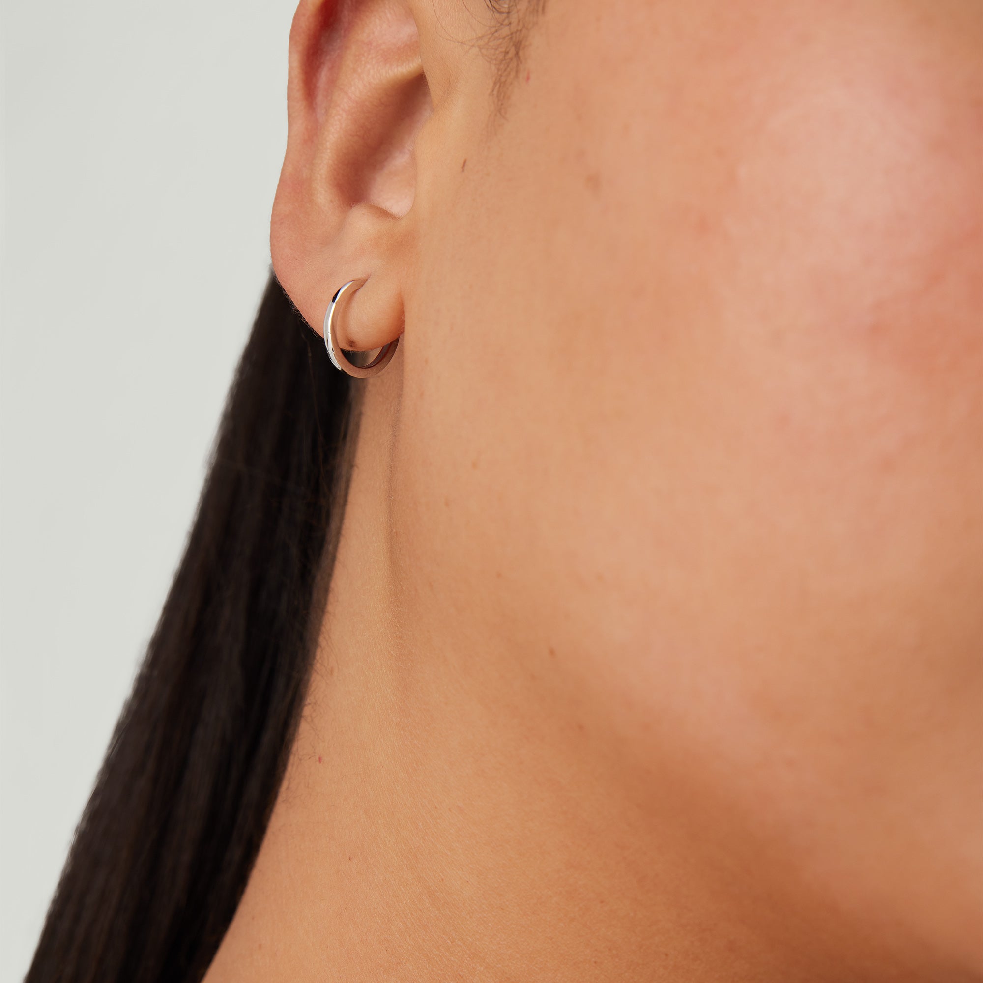 Close-up of a woman's ear wearing the Single Easy Huggie Hoop, a handcrafted 14k gold earring with a clicker closure for comfort and security.