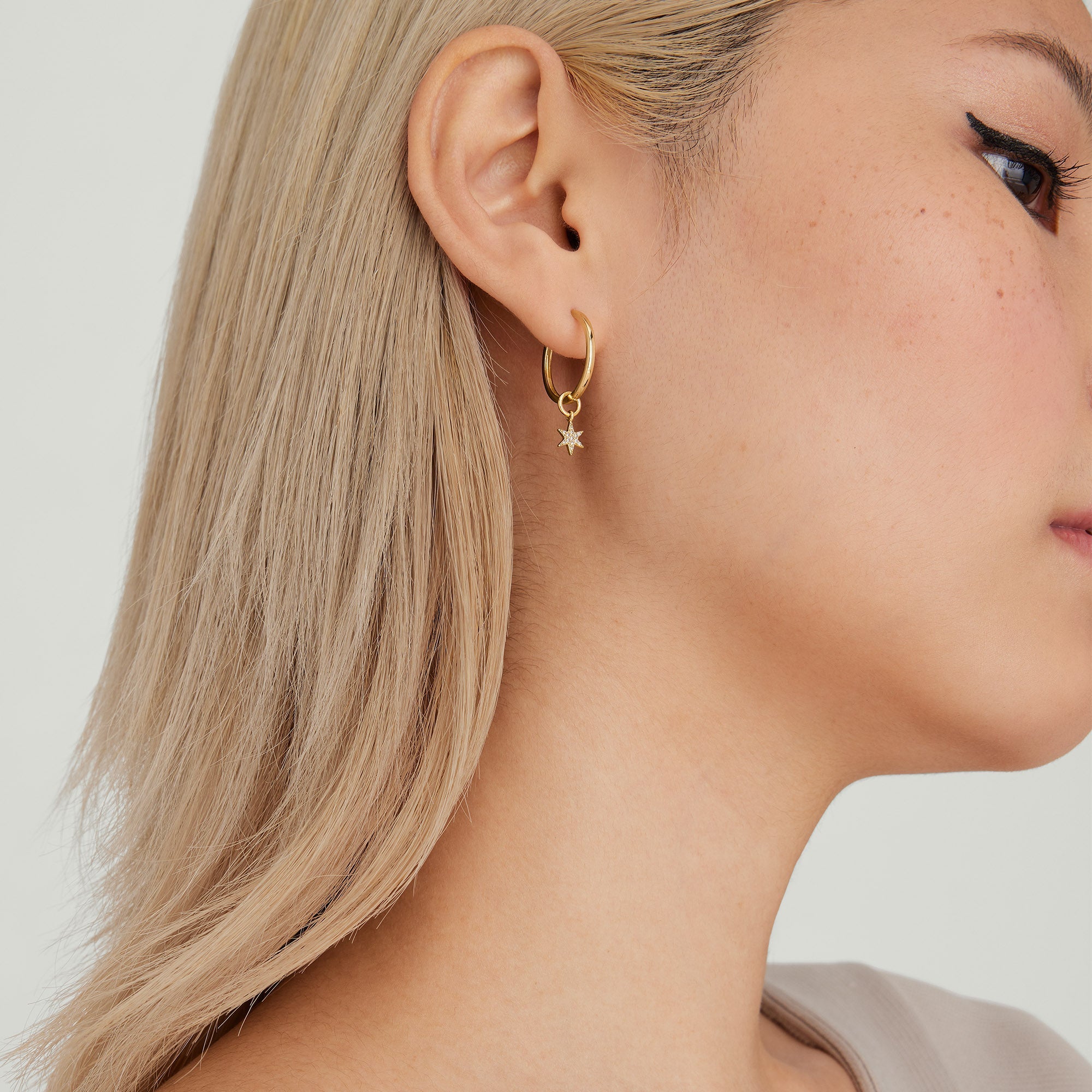 Close-up of a woman's ear wearing a Single PavÃ© Diamond Star Hoop Charm, showcasing the detailed star pendant on a gold hoop earring.