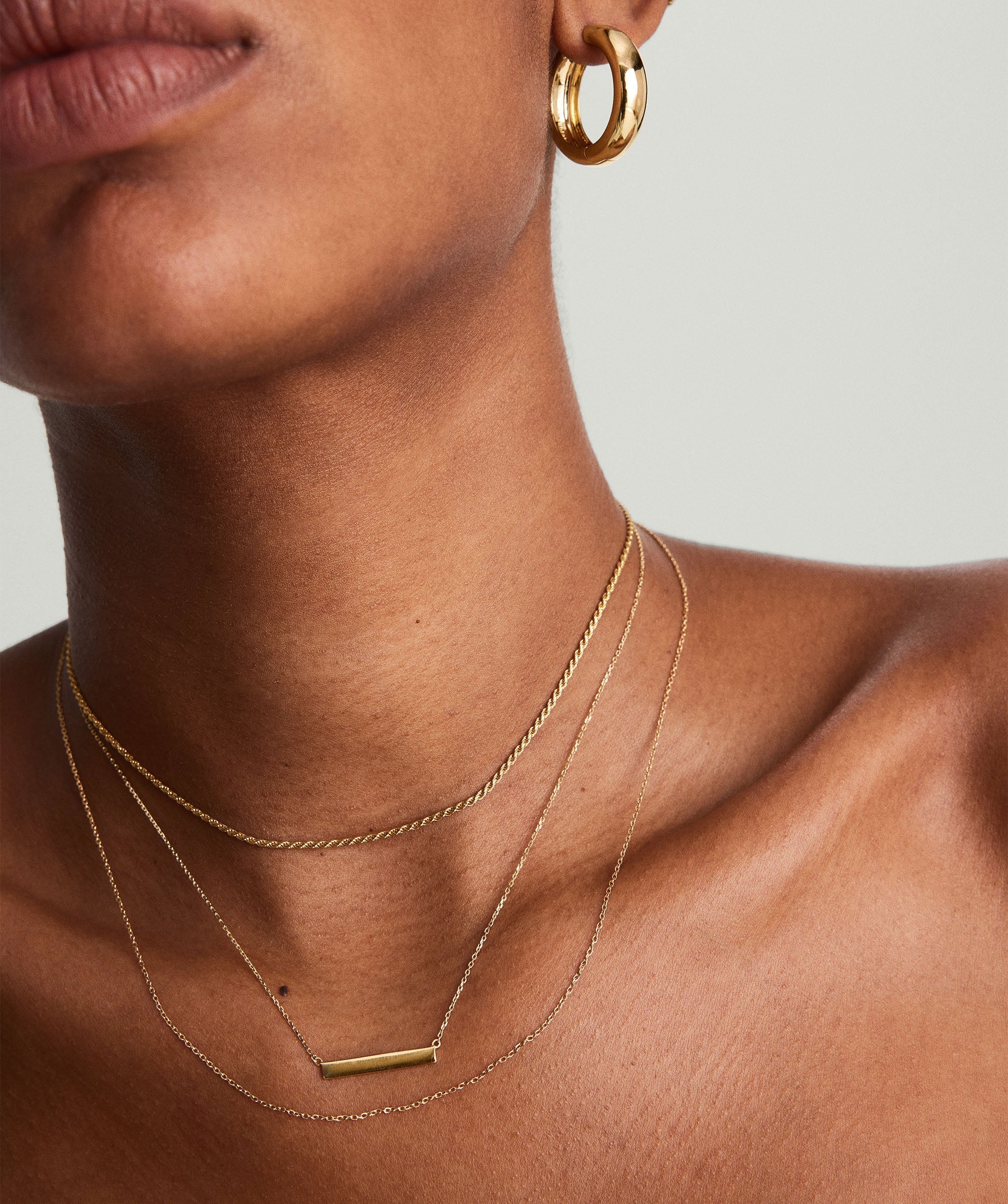 A close-up of a woman wearing the Horizontal Engravable Bar Necklace, a sleek 14k solid gold chain with an engravable bar.