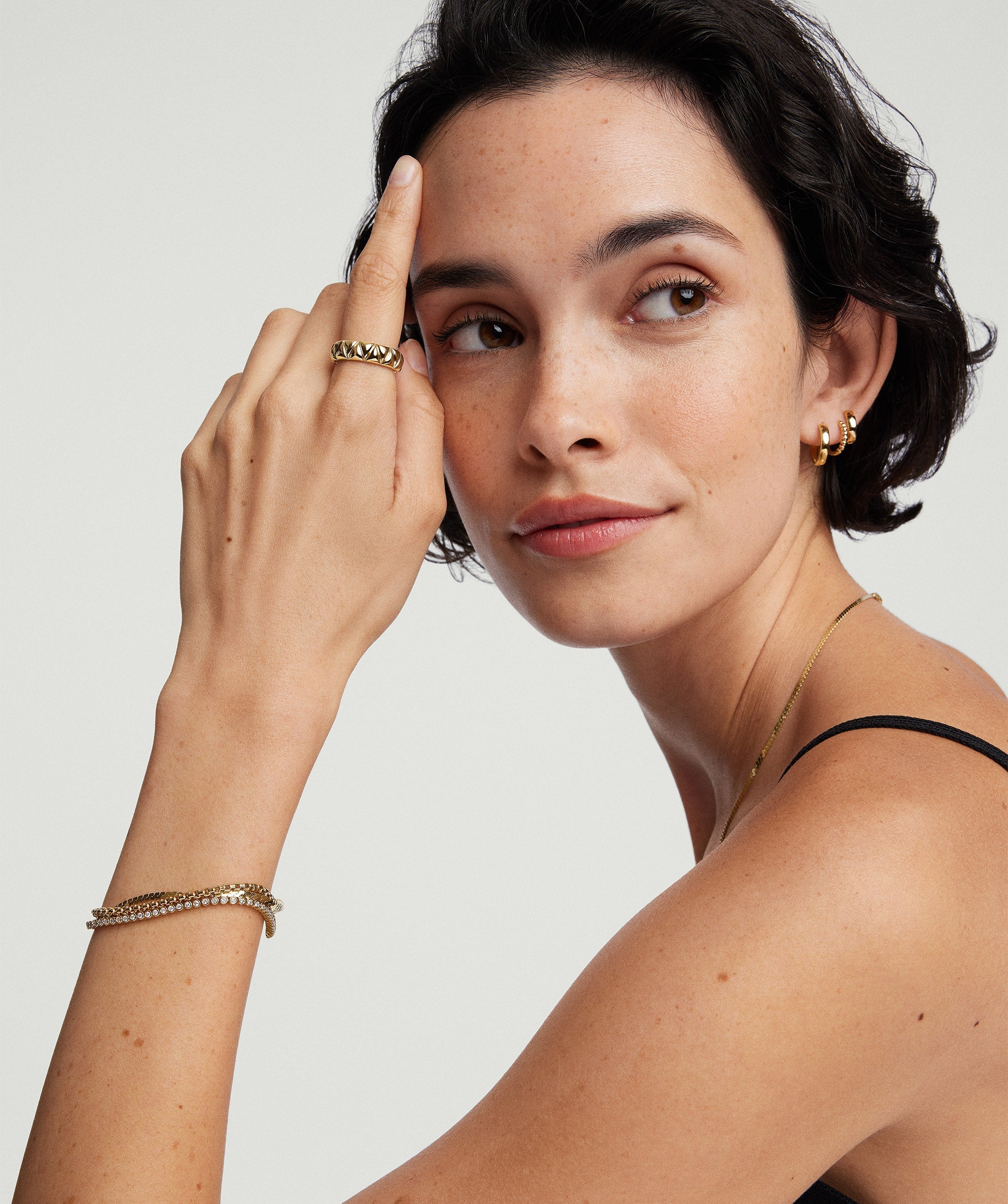 Woman wearing a Bezel Lab Grown Diamond Tennis Bracelet on her wrist, along with gold hoop earrings and a ring.