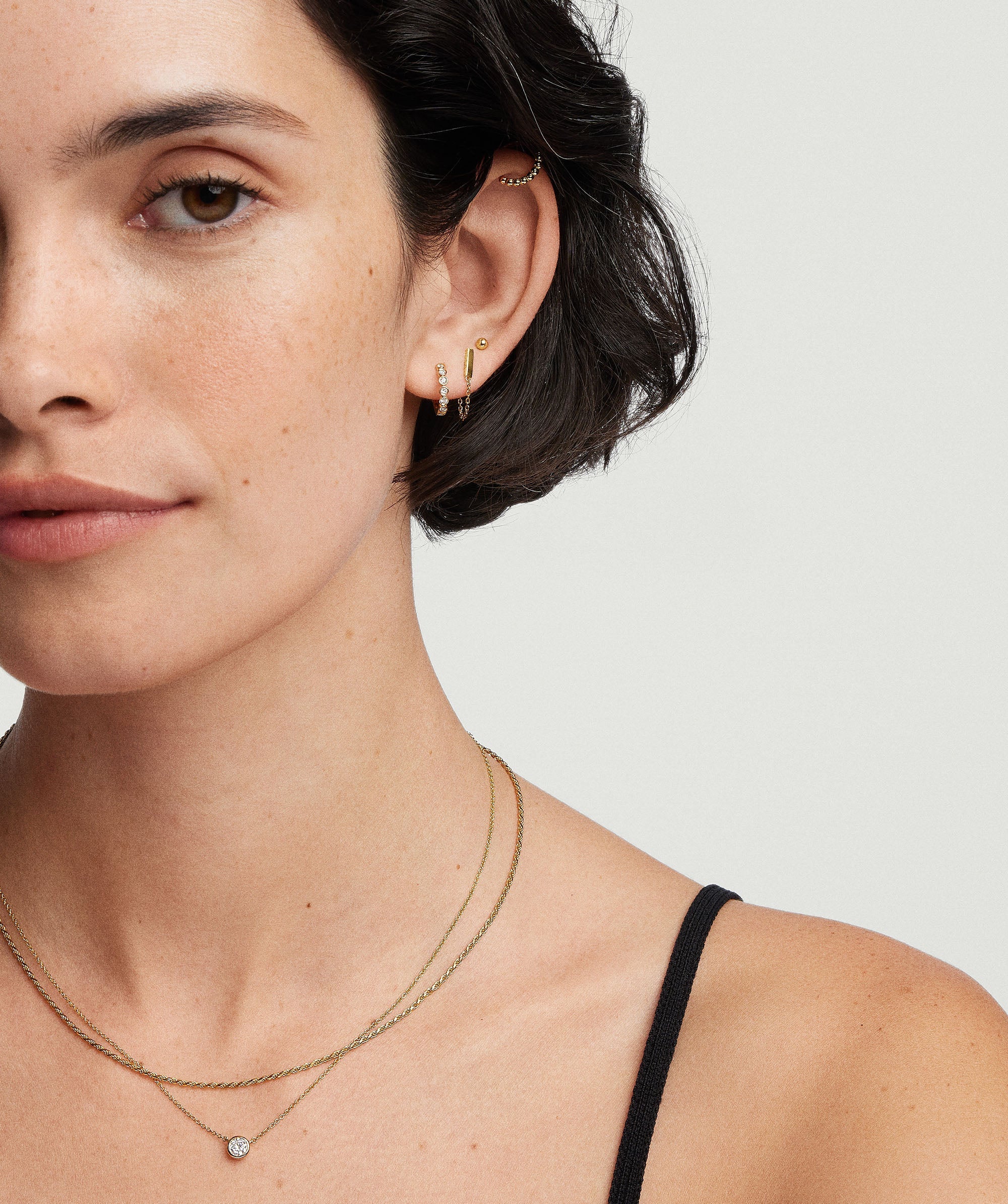 Woman wearing Bezel Lab Grown Diamond Huggies, showcasing sparkling handcrafted 14k solid gold earrings with bezel-set, ethically produced lab-grown diamonds.