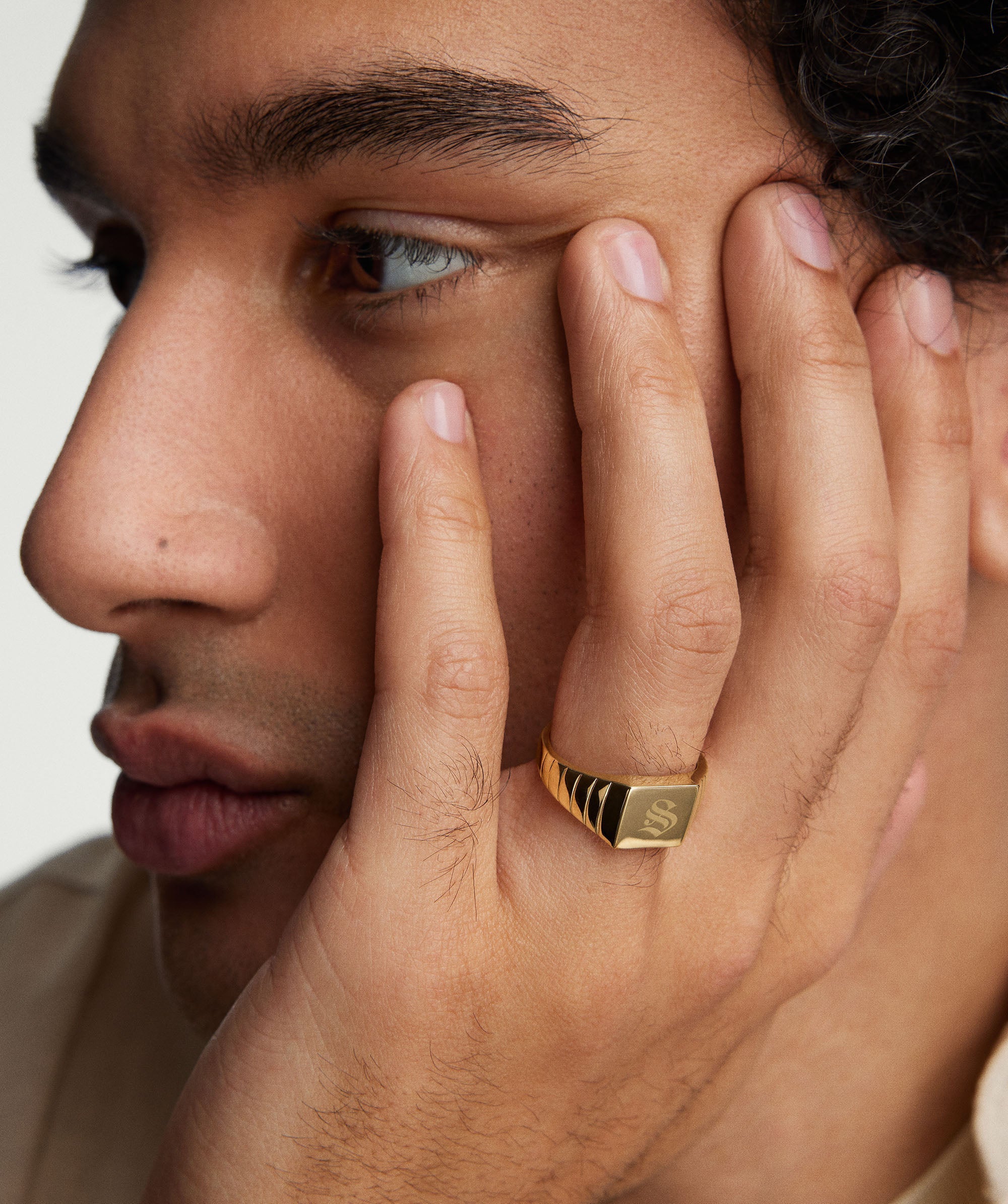 Close-up of a man resting his hand on his face, showcasing a bold Square Signet Ring on his finger.