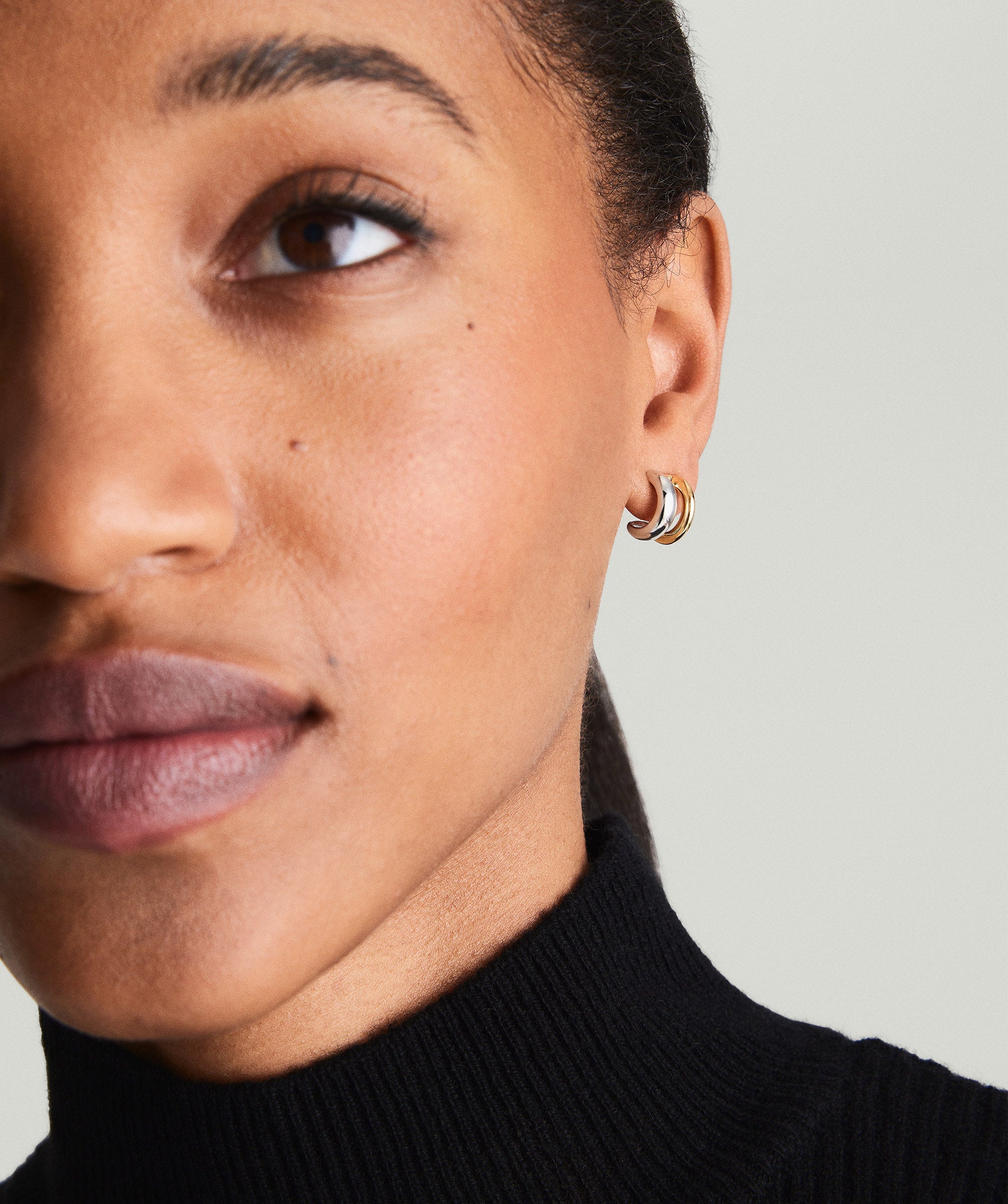 Close-up of Duet Mixed Huggie Hoops on a woman's ear, showcasing dual metal design in 18k gold vermeil and sterling silver.