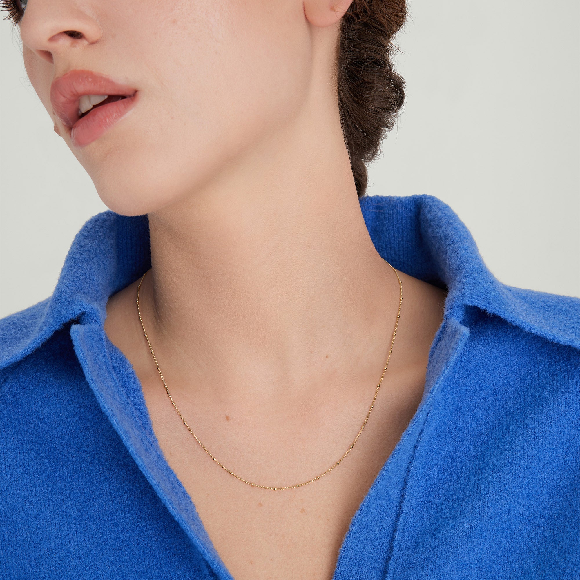 Woman wearing a blue shirt and a minimal Spheres Chain Necklace, making a bold statement. Perfect for any occasion.