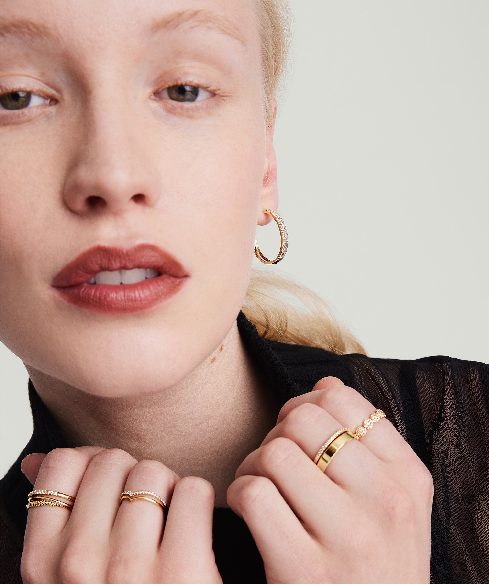 A woman showcasing Bold PavÃ© Diamond Large Hoops, wearing a black shirt, gold rings, and earrings, highlighting the intricate design of the handcrafted 14k gold hoops.