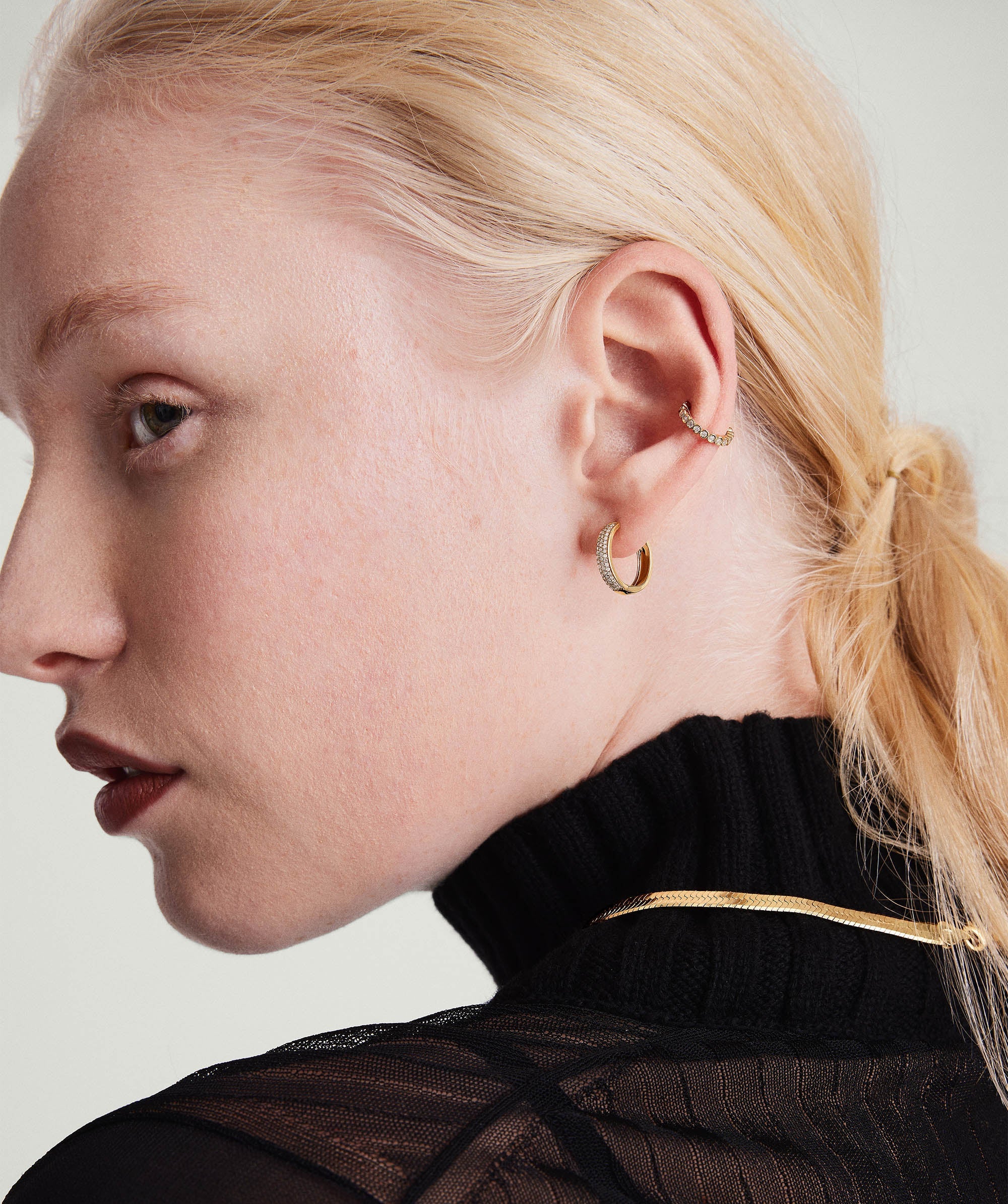 Woman with blonde hair showcasing Bold PavÃ© Diamond Small Hoops, crafted in 14k solid gold with responsibly sourced diamonds, highlighting the earring's intricate design and elegance.