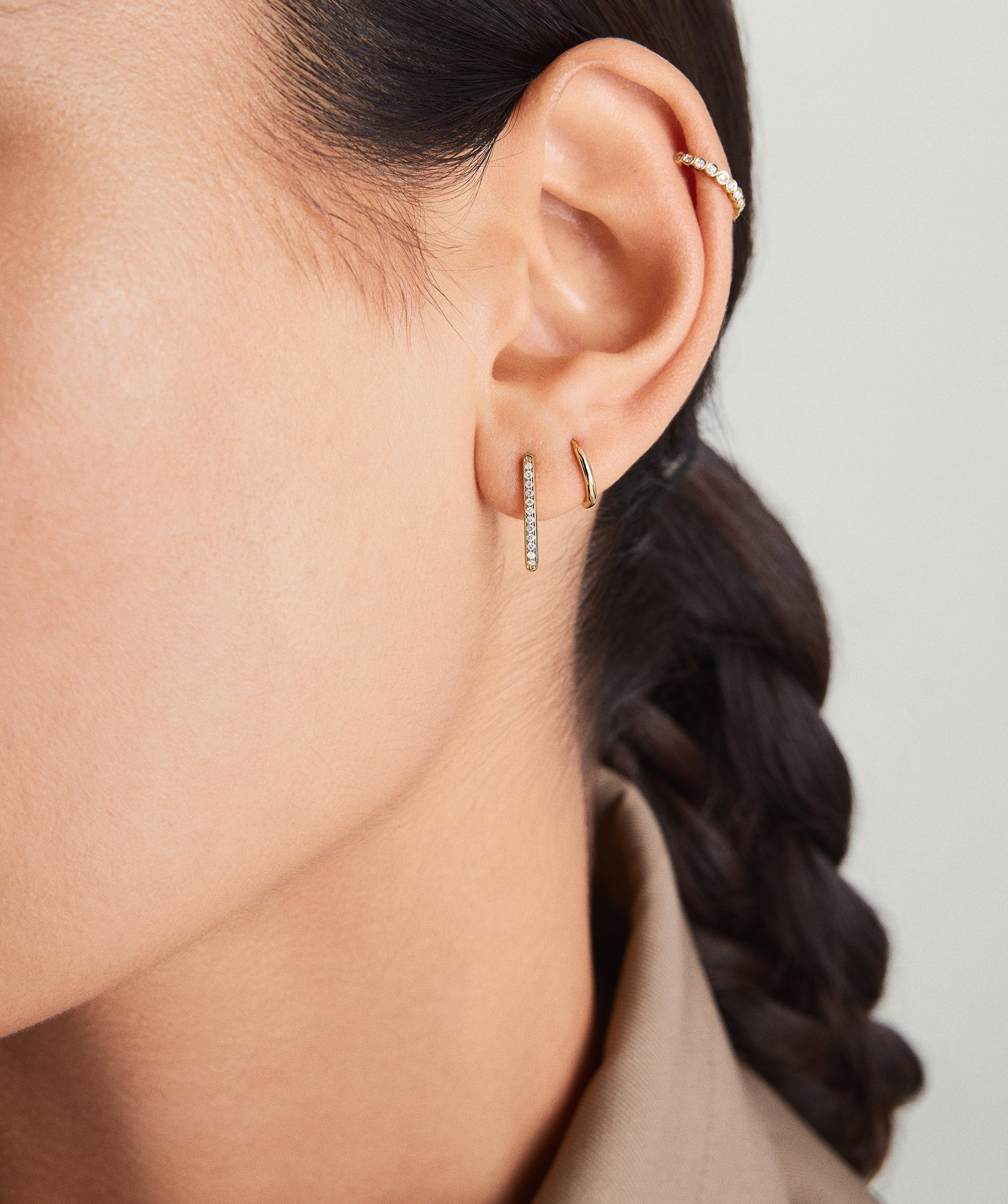 Close-up of a woman's ear adorned with PavÃ© Diamond Small U Hoops, featuring handcrafted 14k gold and responsibly sourced diamonds.