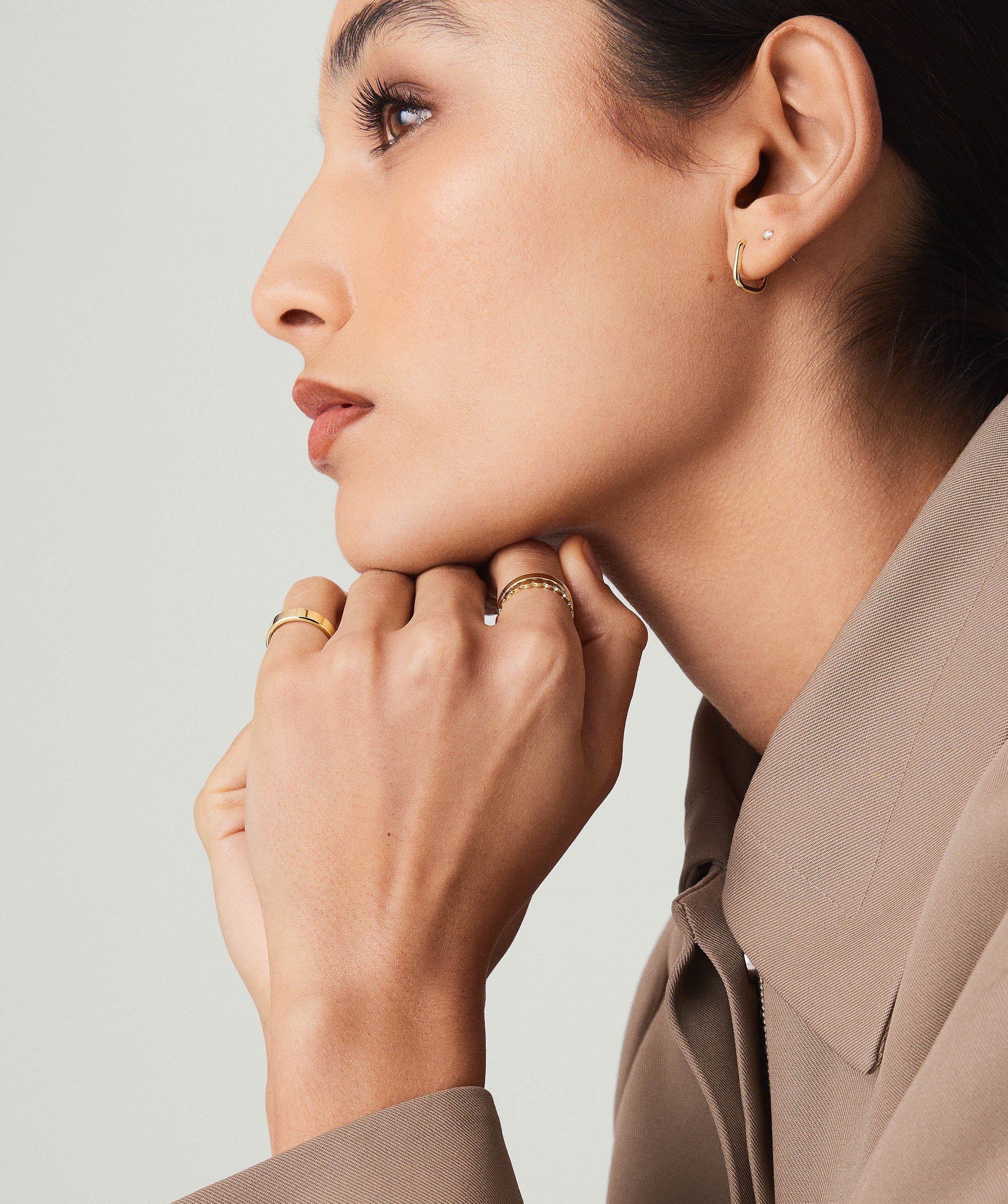 Close-up of a woman wearing Huggie U Hoops, 14k solid gold earrings with sparkly diamonds, hands resting on chin.