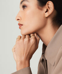Close-up of a woman wearing Huggie U Hoops, 14k solid gold earrings with sparkly diamonds, hands resting on chin.