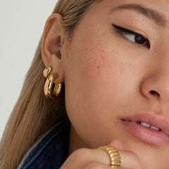 Close-up of a woman's ear showcasing Chunky Huggie Hoops with a clicker closure, emphasizing the earrings' pillowy texture and stackable design.