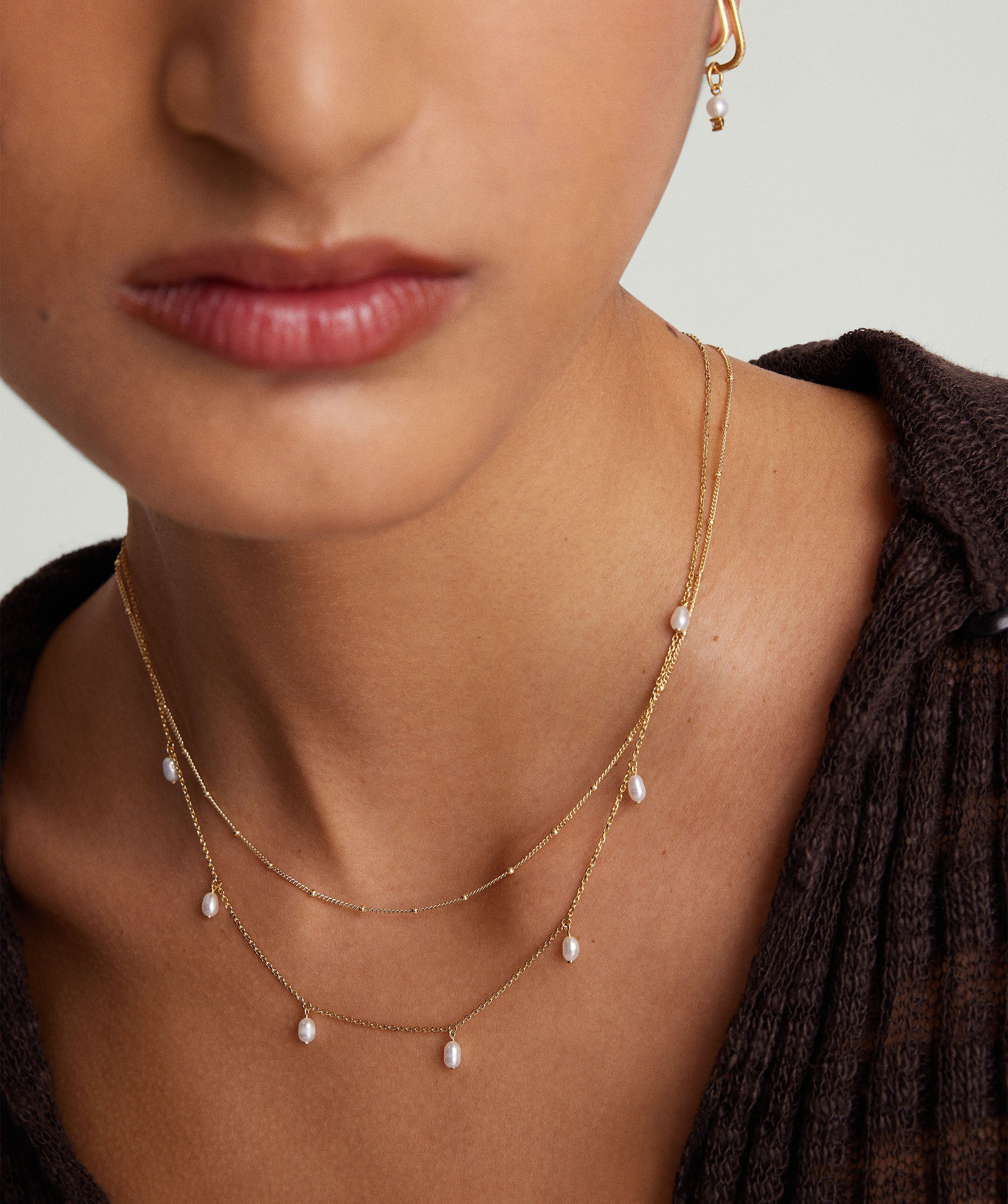 A woman wearing the Tiny Pearl Station Necklace, handcrafted in 18k gold vermeil with freshwater pearls, shown close-up on her neck.