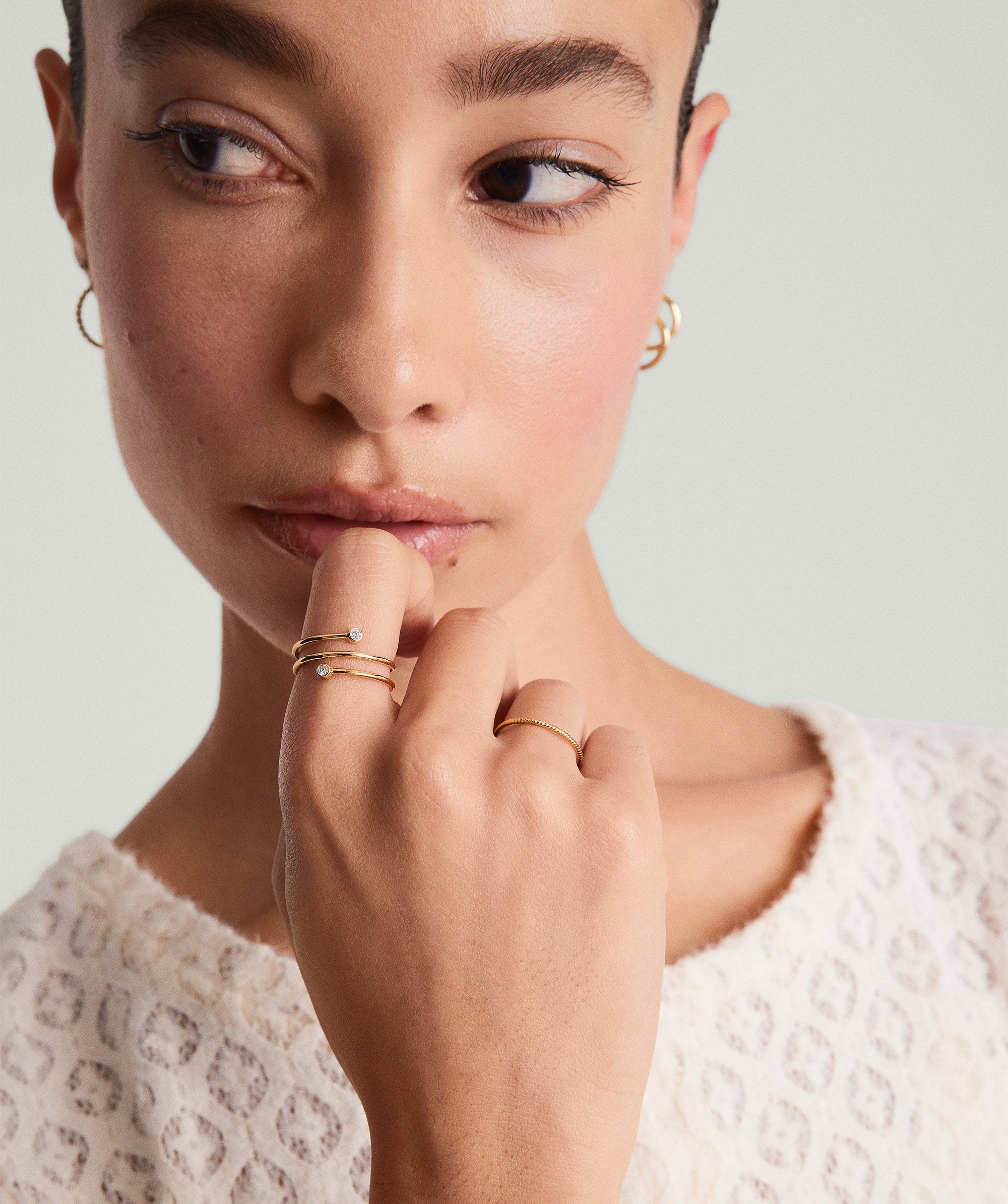 Diamond Coil Ring on a woman's finger, featuring multiple intertwined bands adorned with pavÃ© diamonds, showcased in a close-up of her hand near her lips.