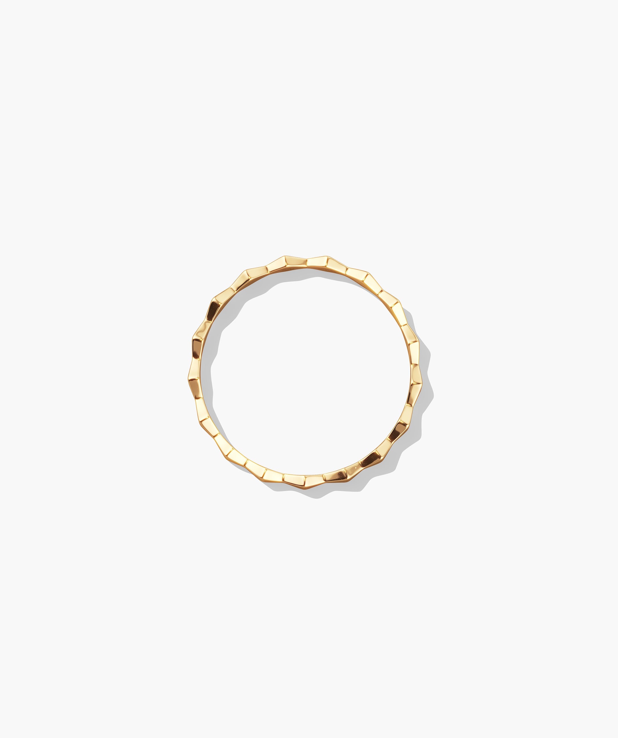 Sculpture Ring: A thin gold bangle with a subtly faceted, hammered surface, photographed flat on a white background, ideal for wearing solo or stacked.