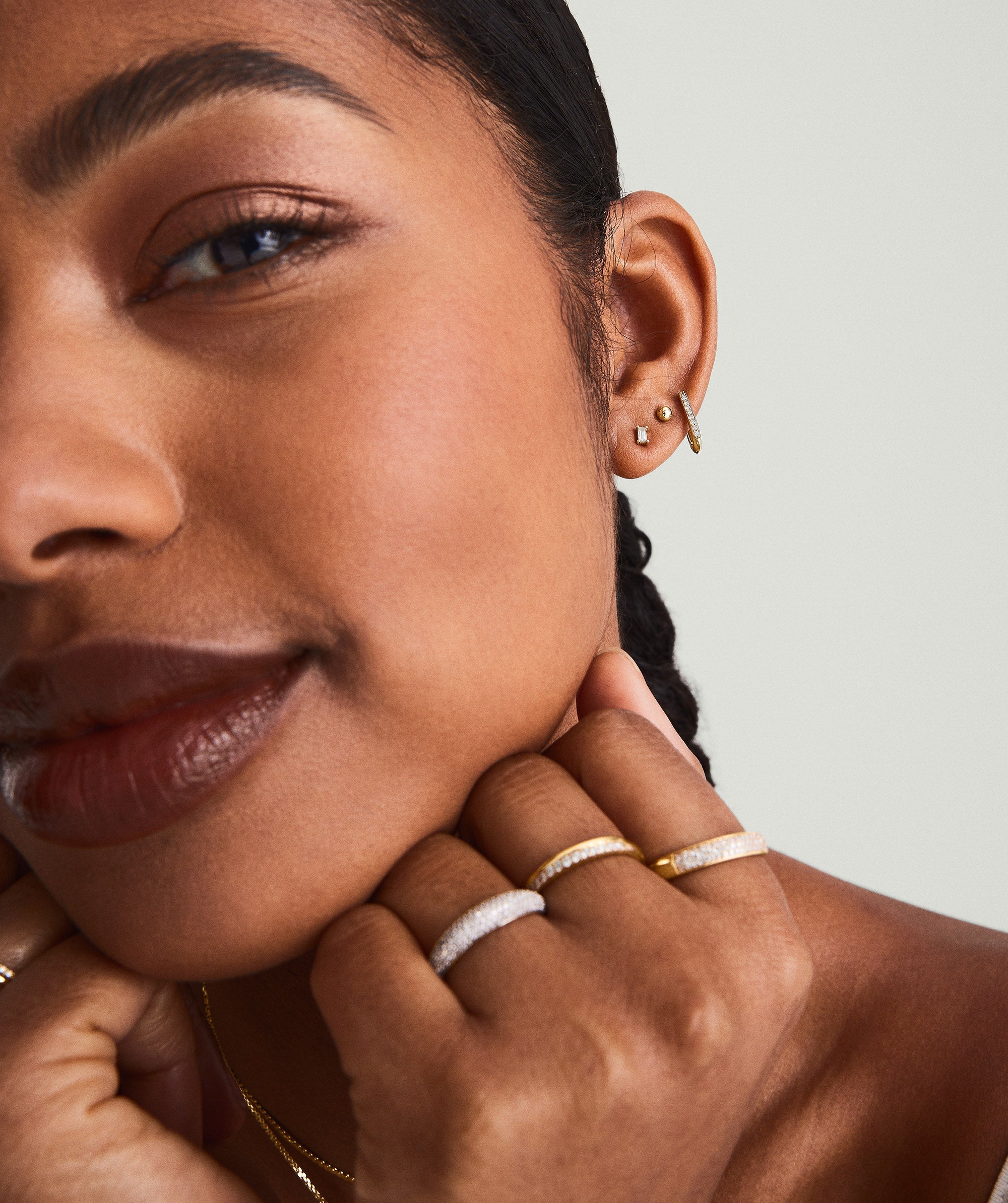 Close-up of a woman's ear wearing a Mini Baguette Diamond Stud earring, handcrafted in 14k solid gold with a responsibly sourced diamond.